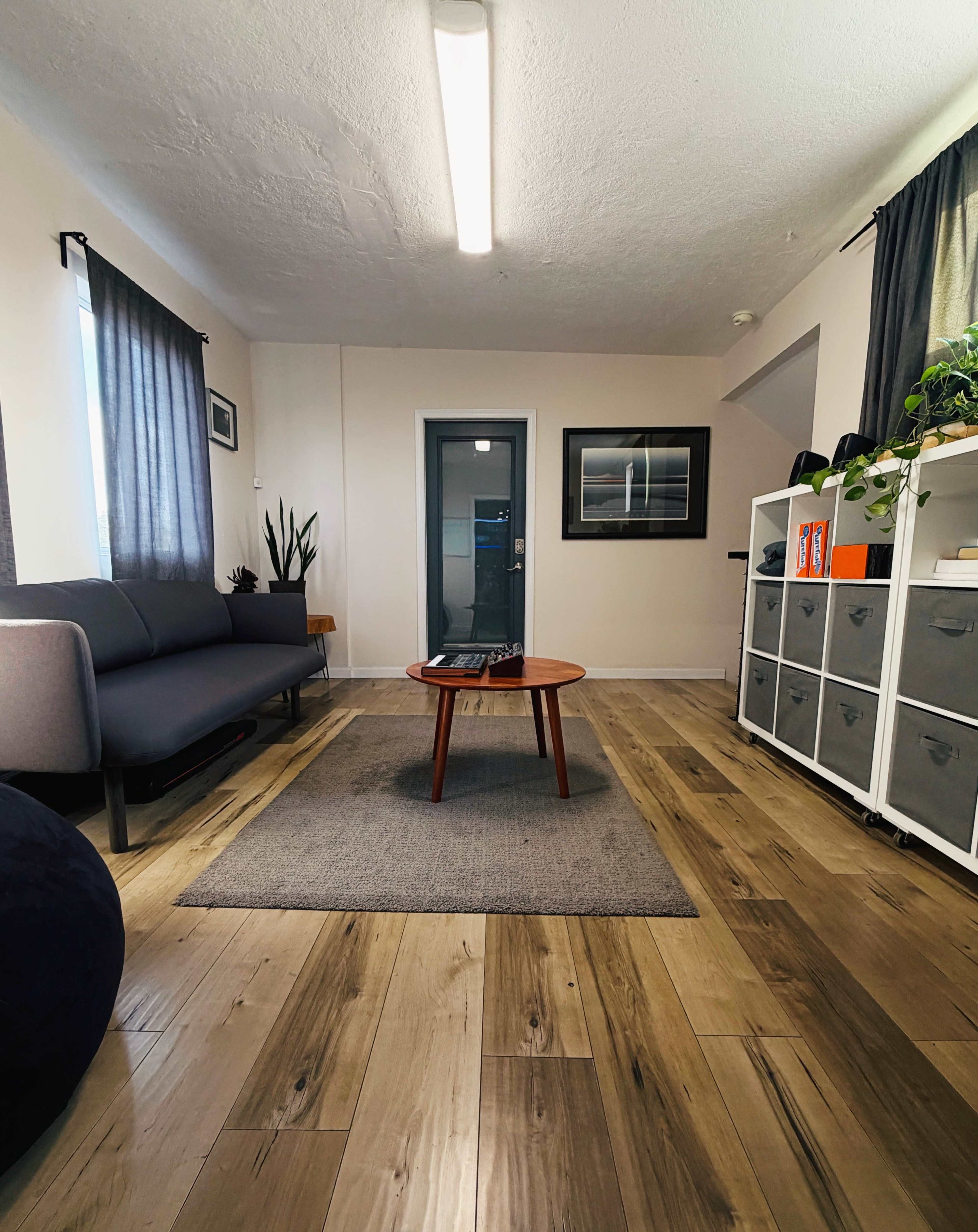 The image shows a modern living room with a gray sofa, a round coffee table on a rug, and storage units against the wall.