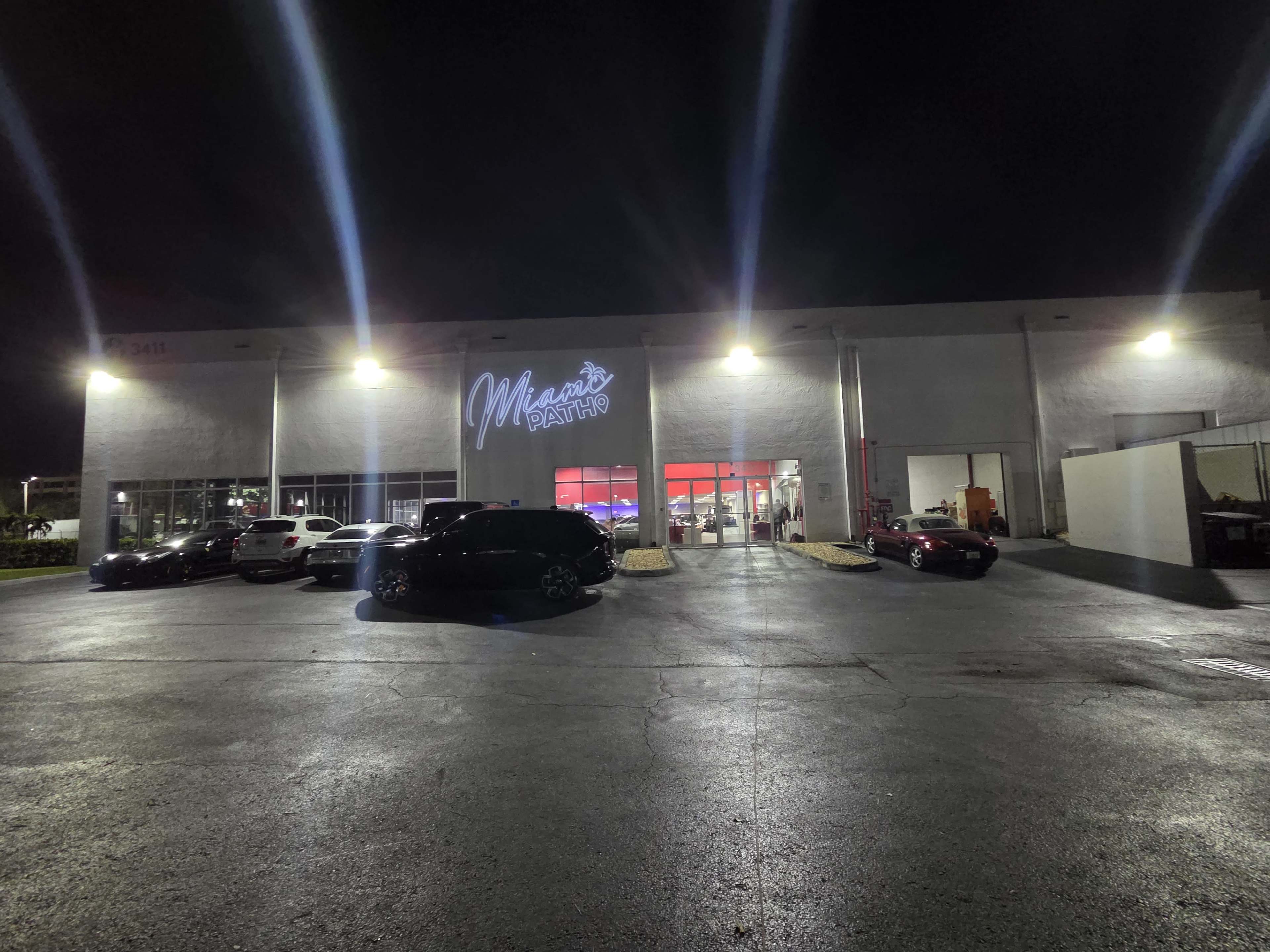 The image shows a dimly lit auto repair shop with several cars parked in front and bright lights illuminating the building.