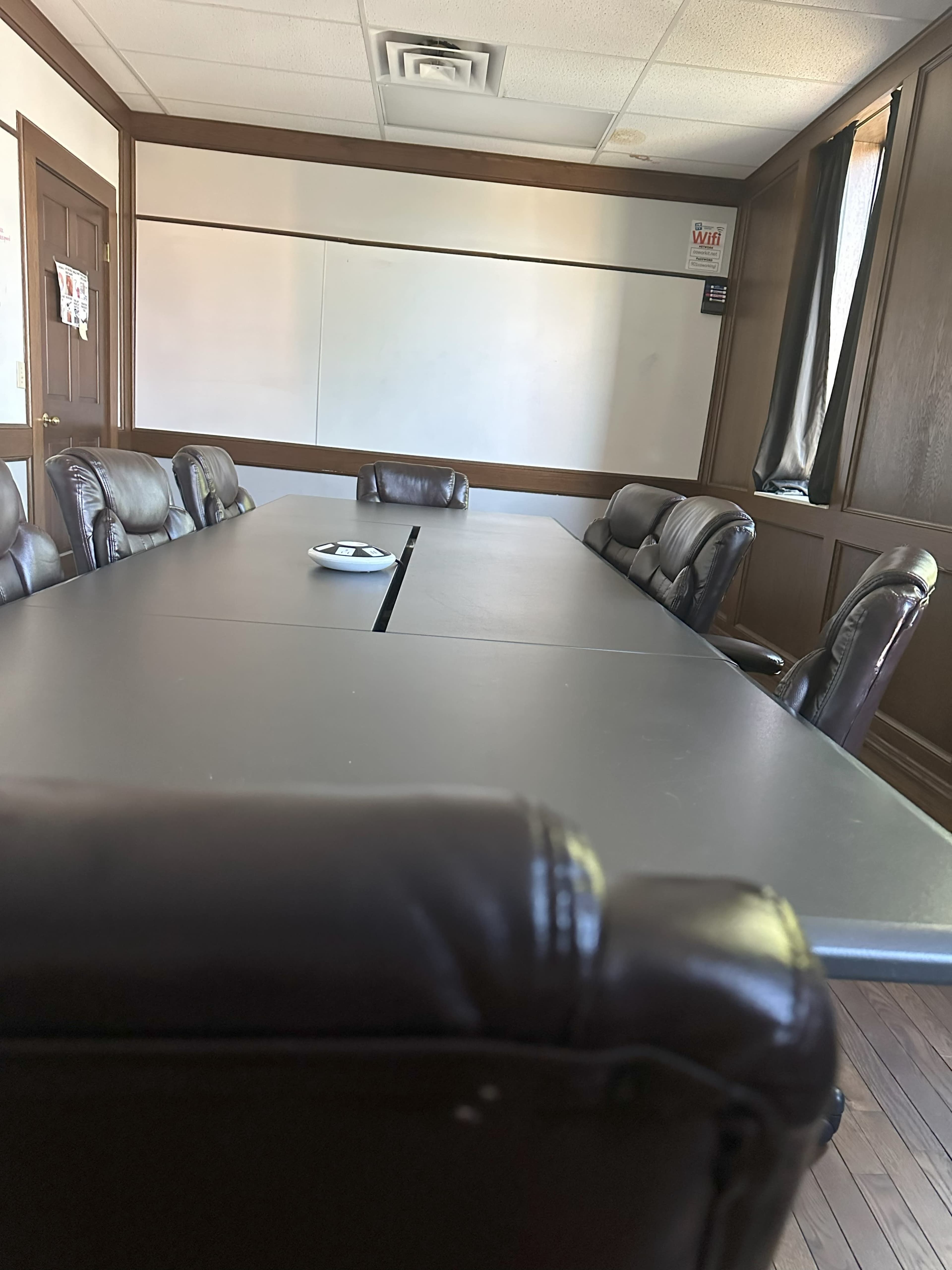 A conference room with a large rectangular table surrounded by leather chairs and a whiteboard in the background.