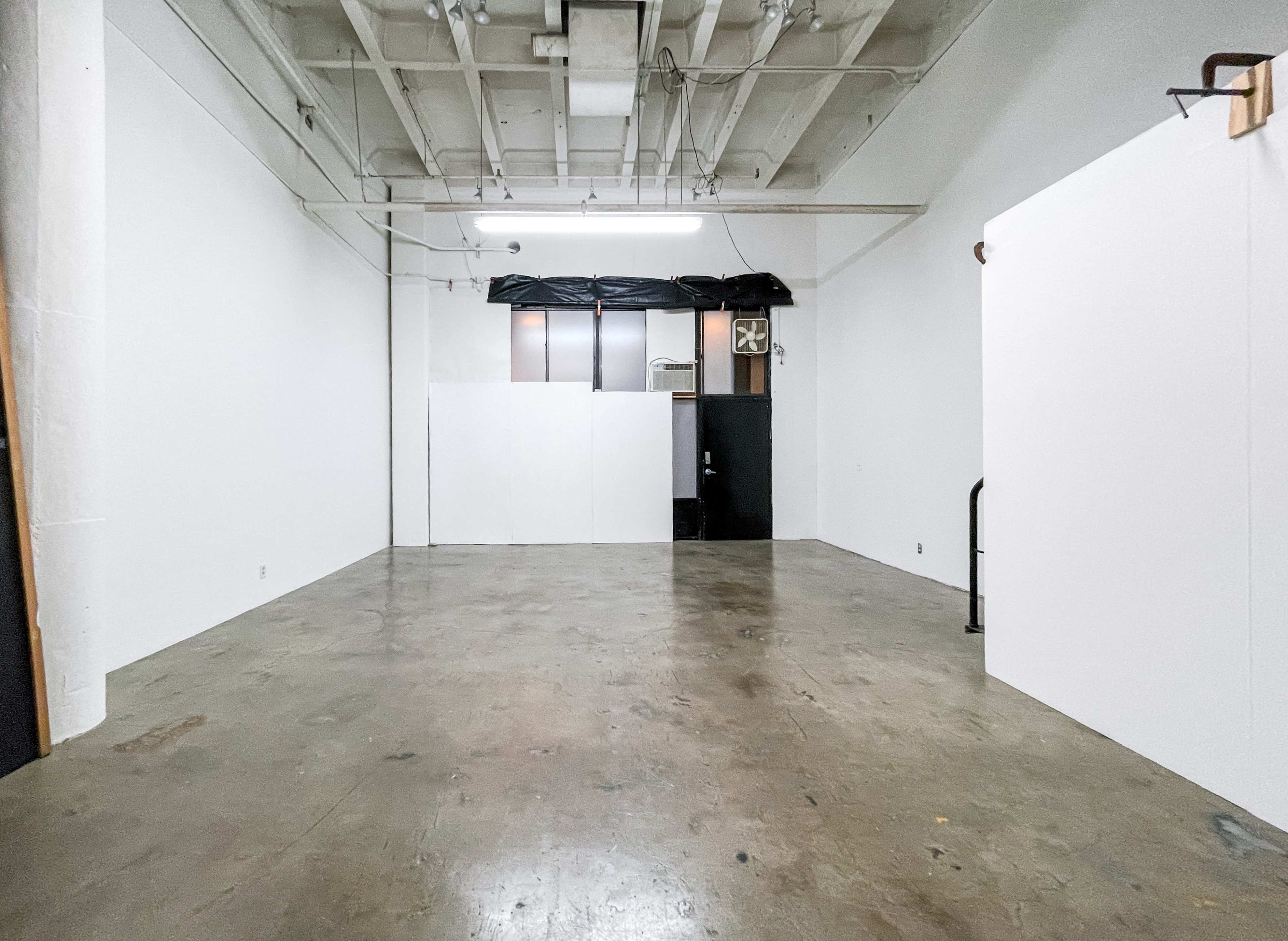 The image shows an empty, spacious room with white walls and a concrete floor.