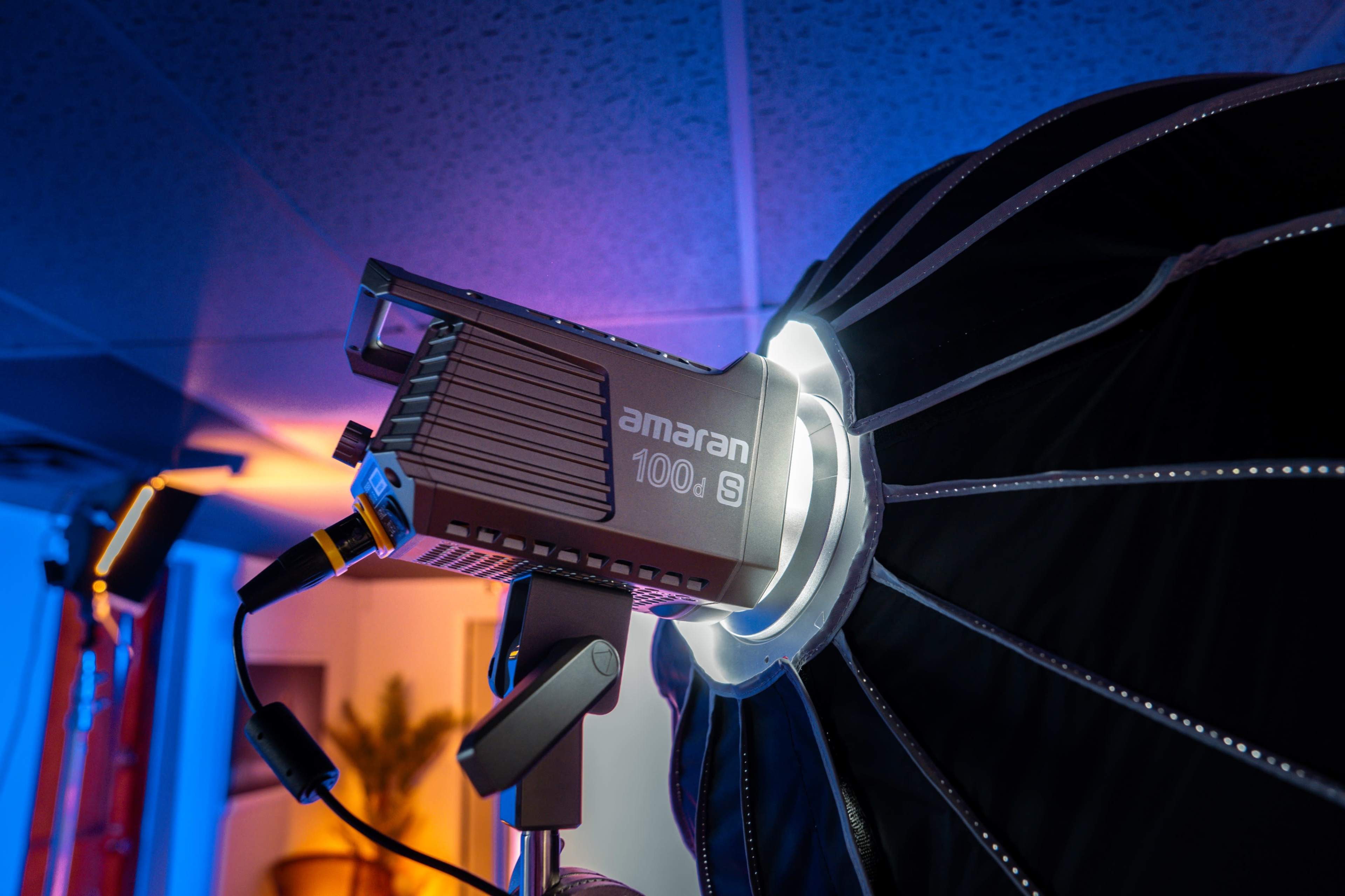 The image shows an Amaran 100S lighting unit mounted on a stand, positioned next to a large softbox with a circular design.