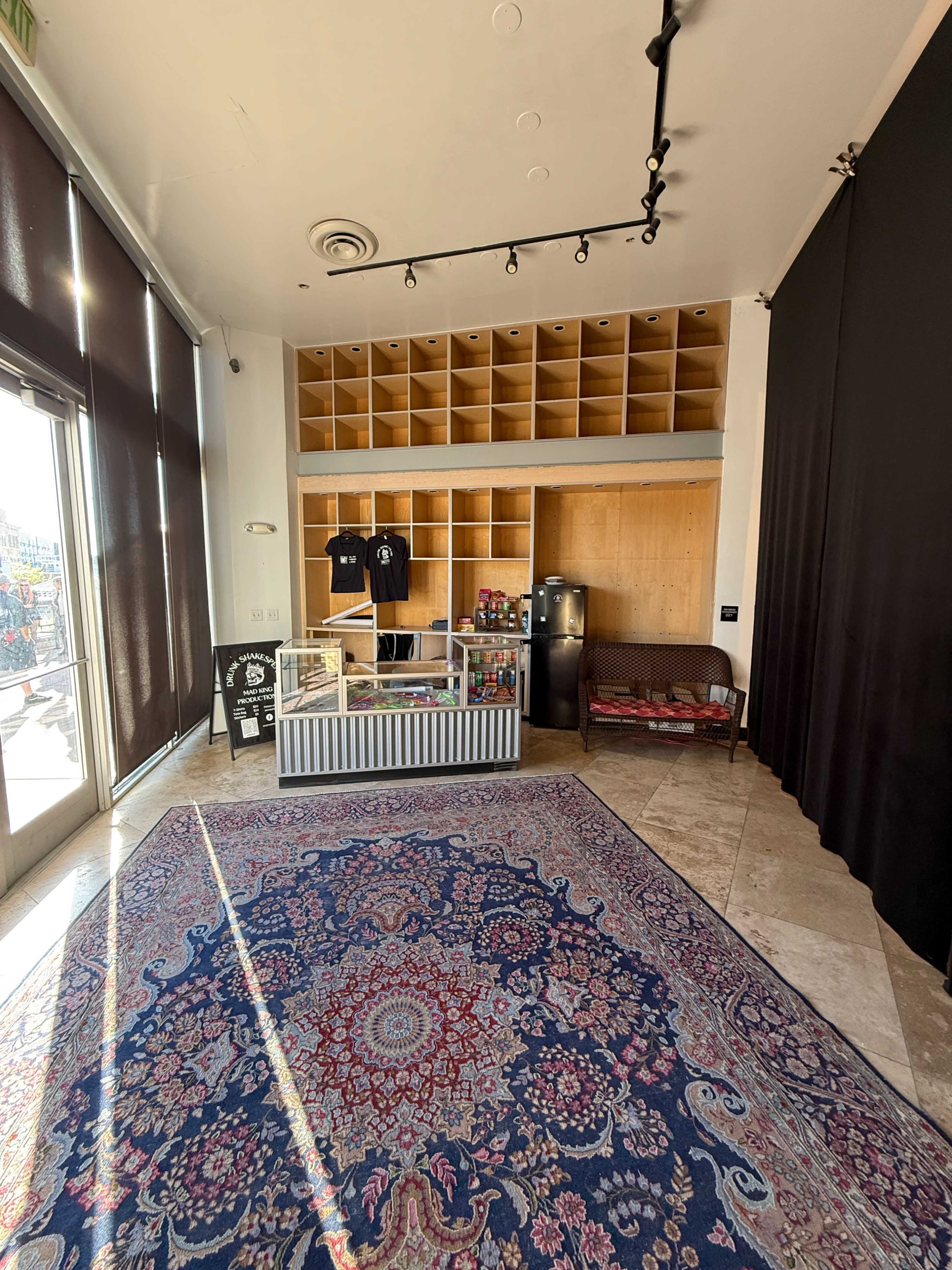The image shows a spacious room with a patterned rug, a display counter, shelving above, and a couch in the corner.