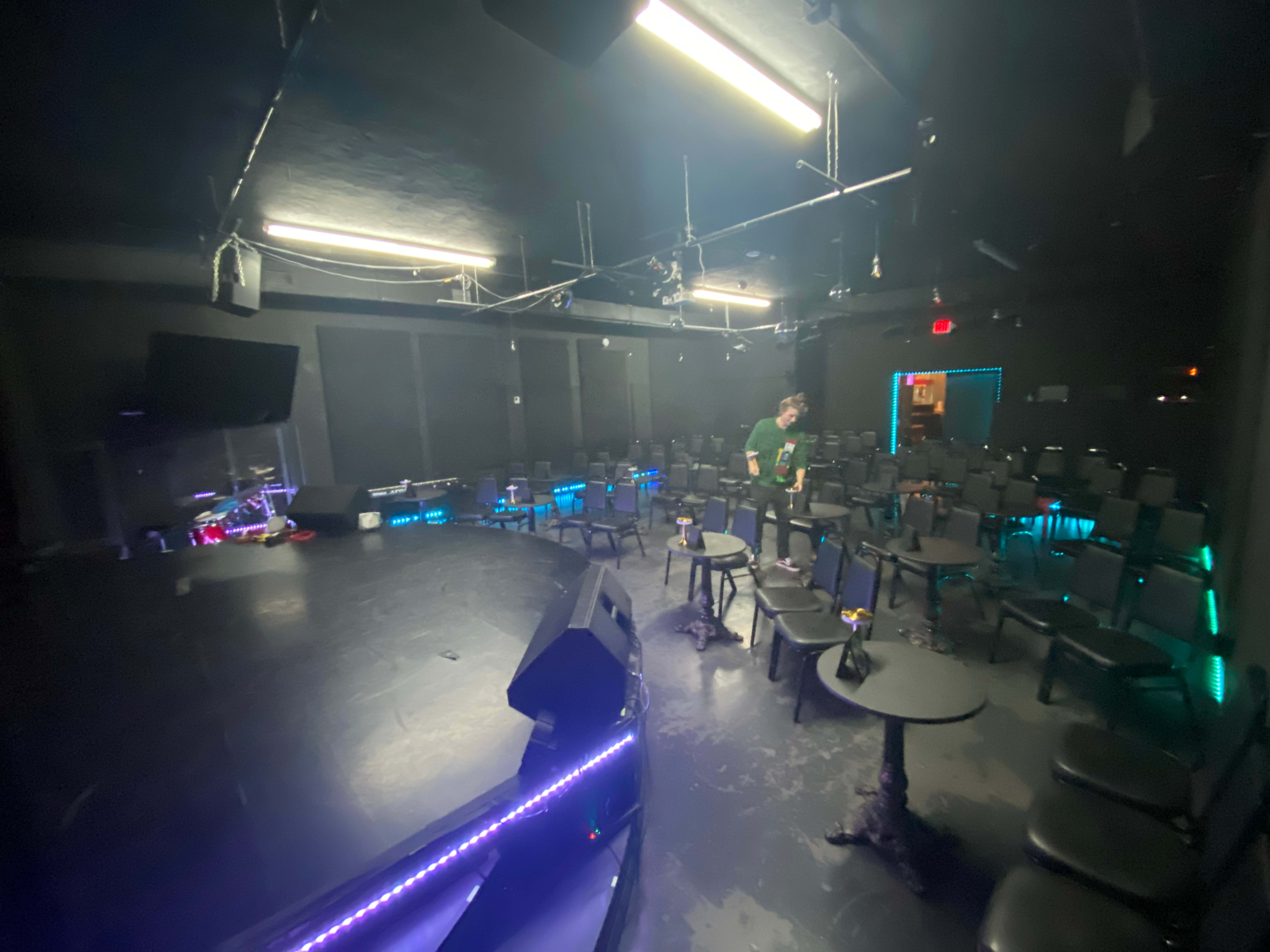 A dimly lit performance space with a circular stage and rows of black chairs arranged for an audience.