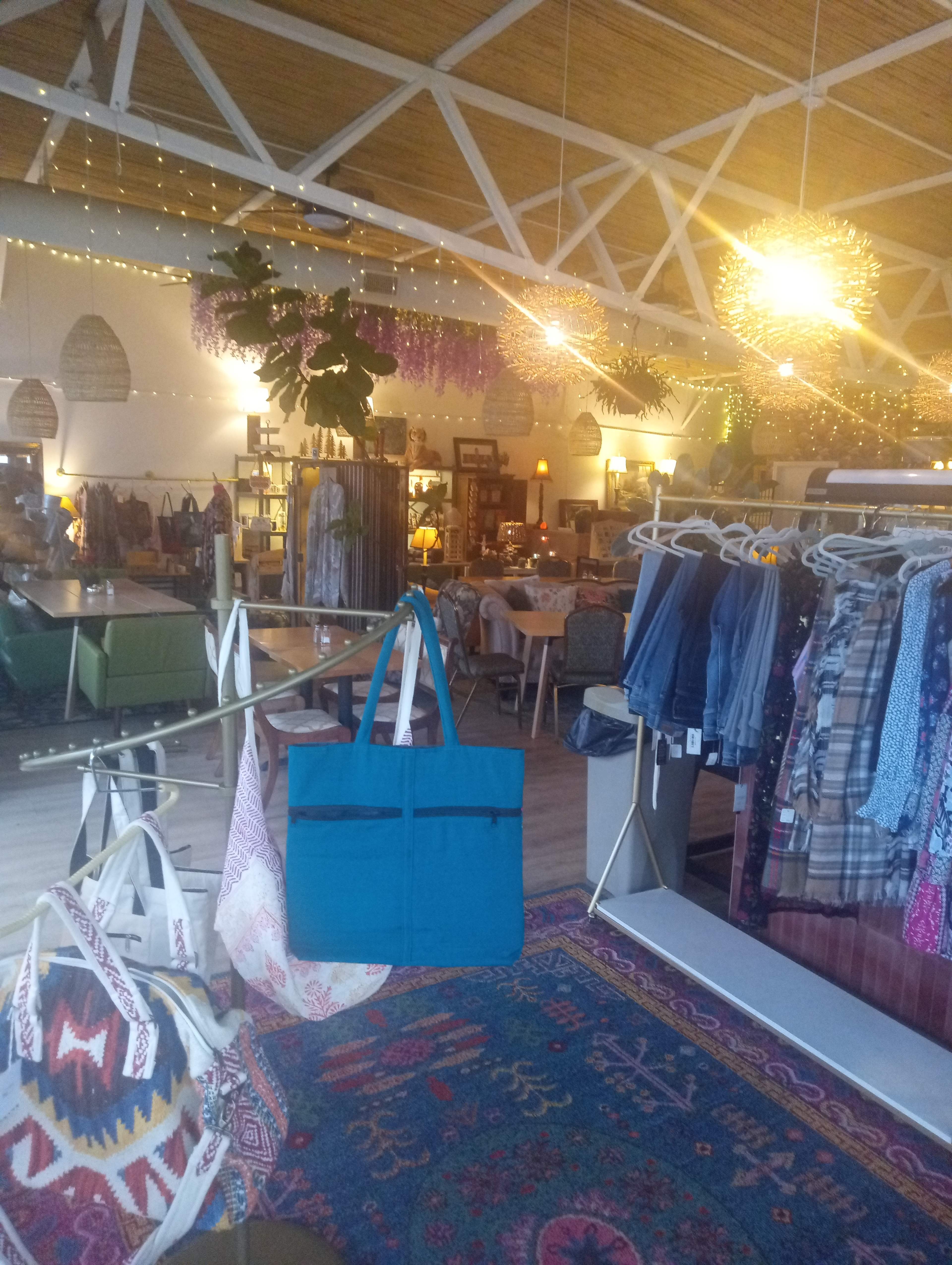 The image shows a spacious retail space featuring colorful clothing and accessories, with hanging lights and decorative plants.
