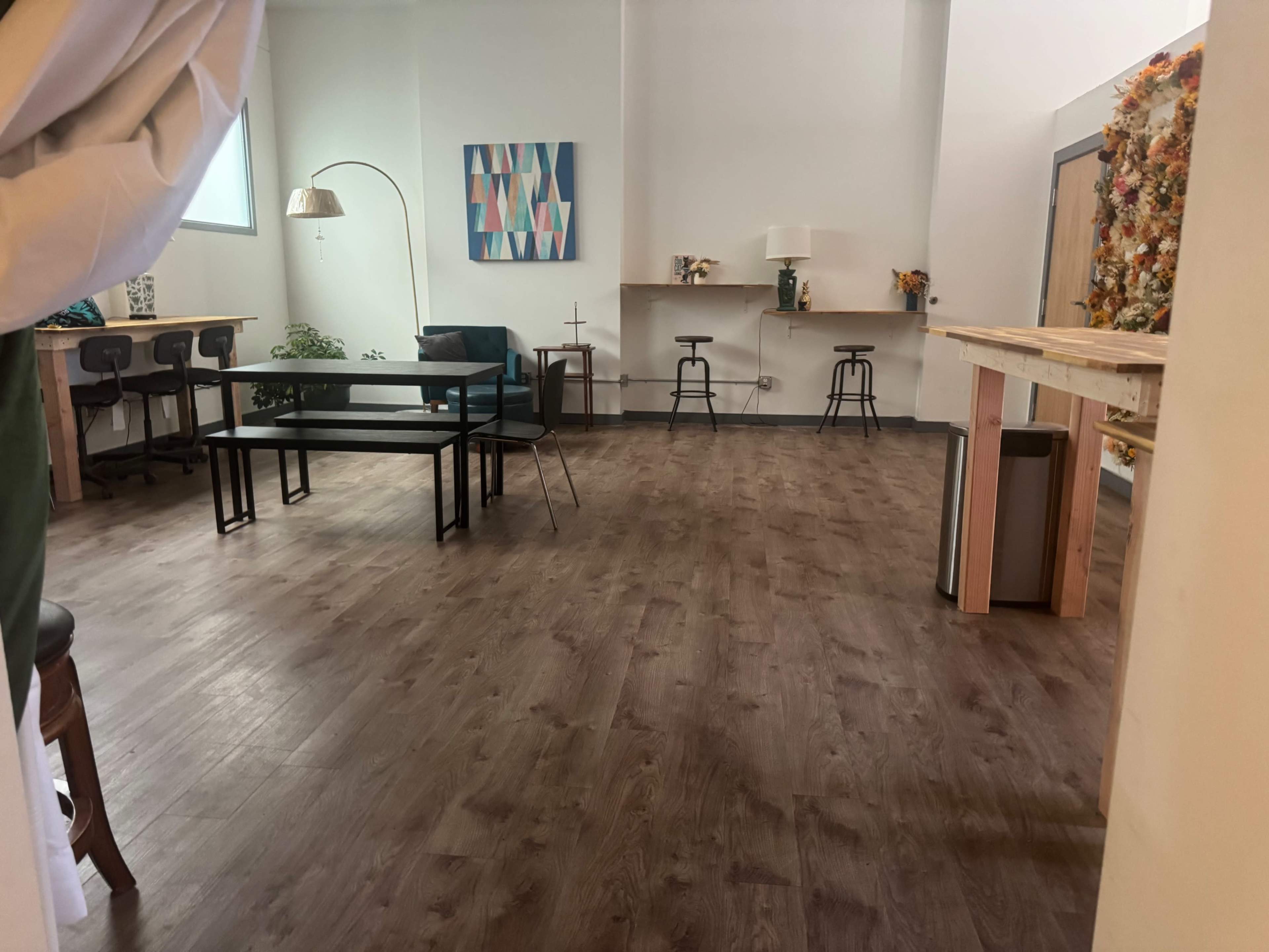 The image shows a spacious, modern interior featuring wooden flooring, a few tables and chairs, and a decorative wall.