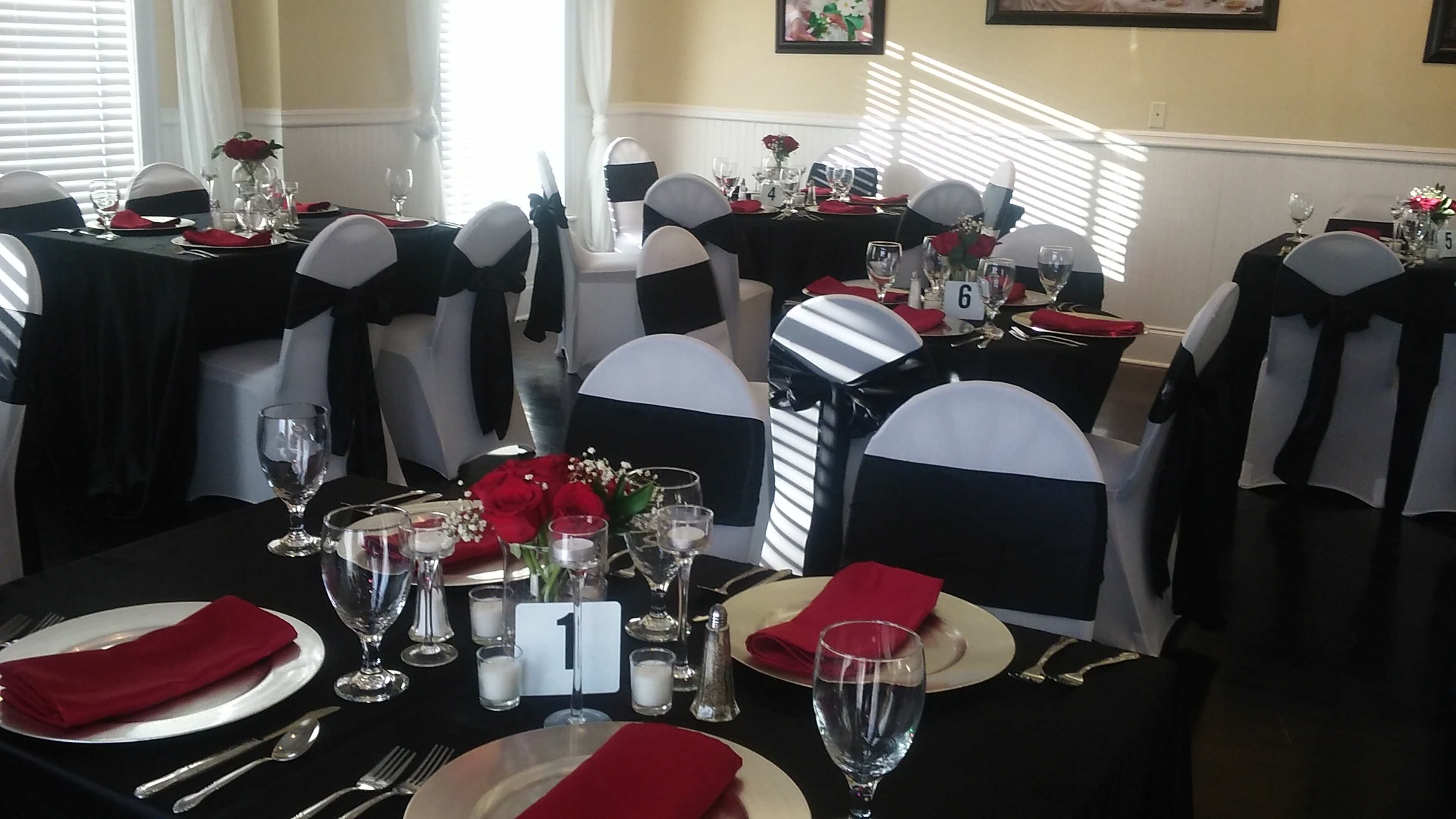 A banquet hall set up with black and white tablecloths, red napkins, and centerpieces of roses and candles on each table.
