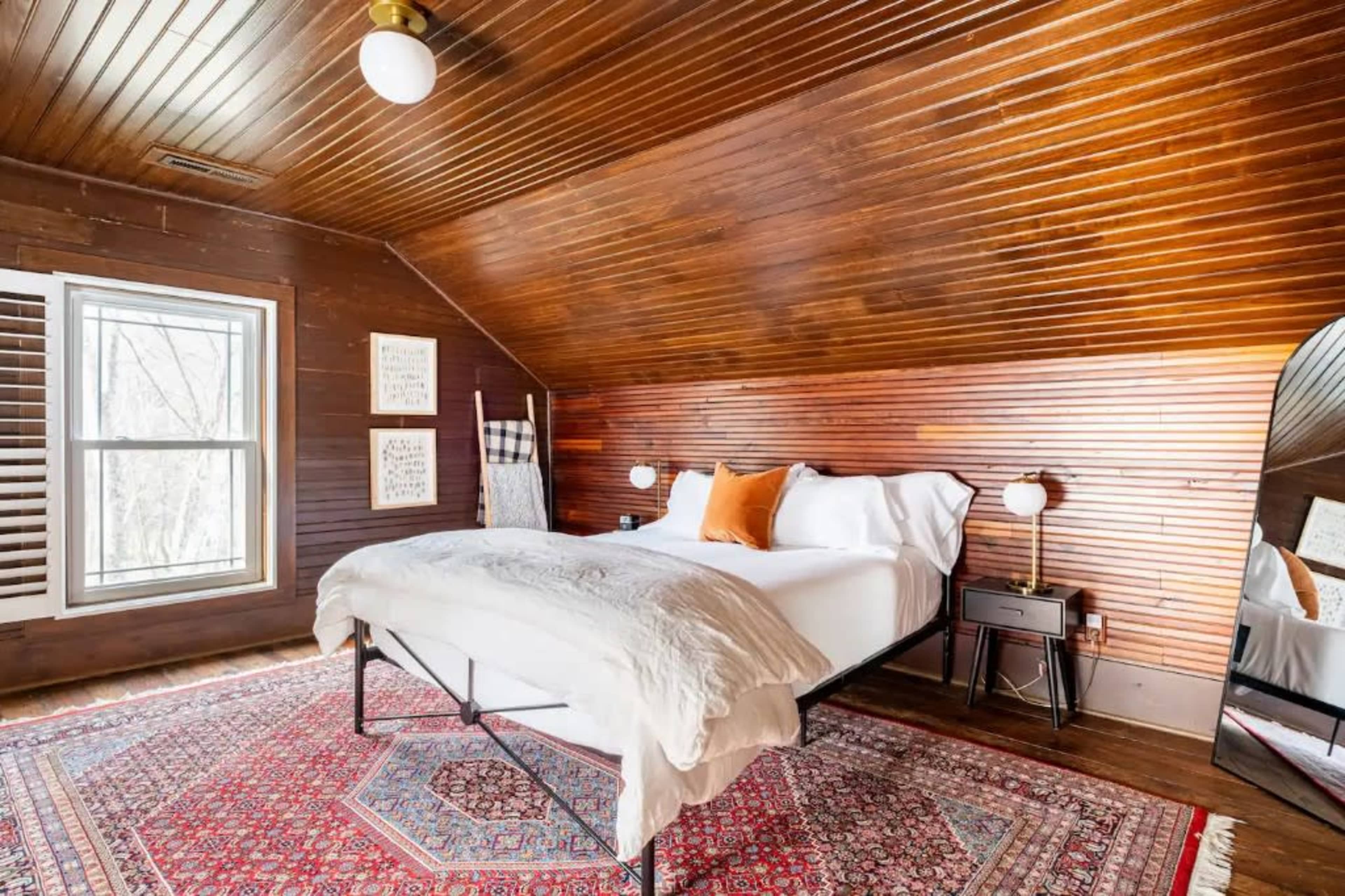 A cozy attic bedroom with a wooden sloped ceiling, a queen-sized bed, and a large mirror against the wall.