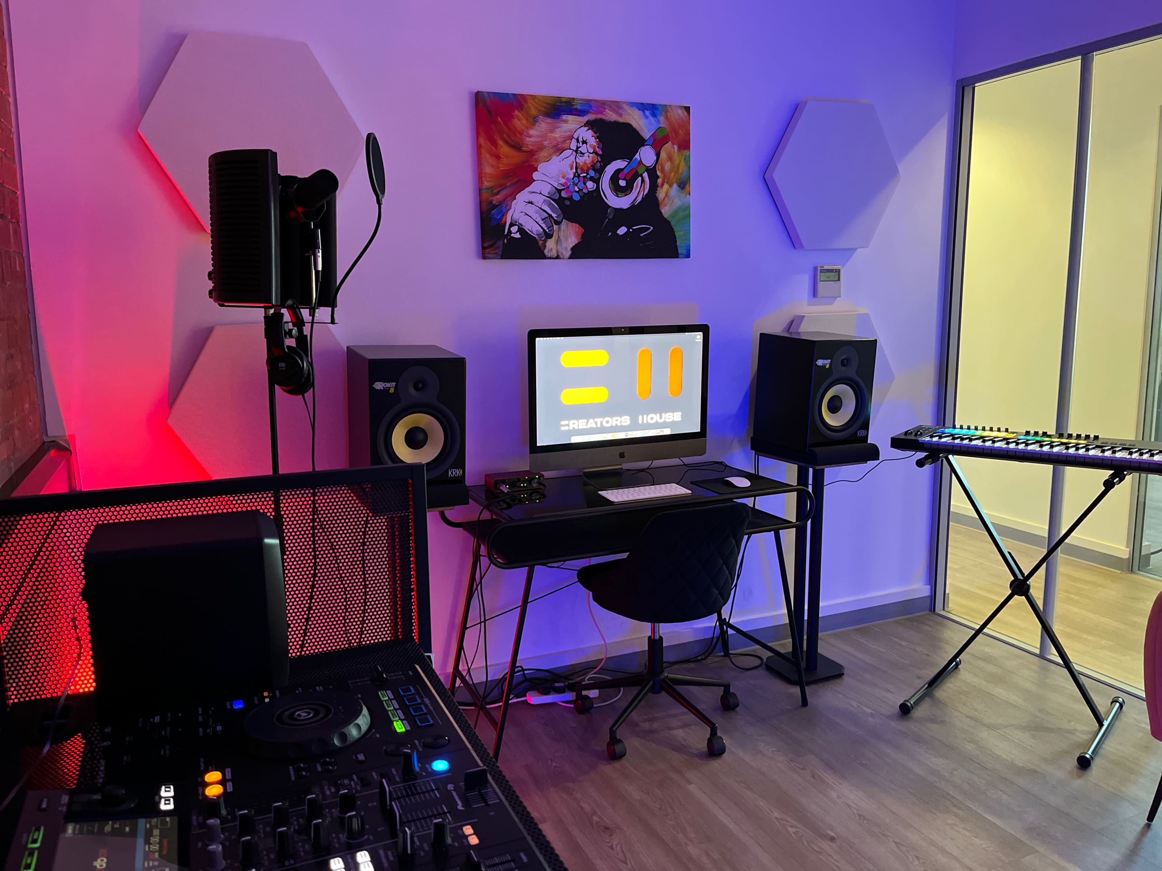 A modern music production studio with a computer, speakers, a digital keyboard, and colorful lighting.