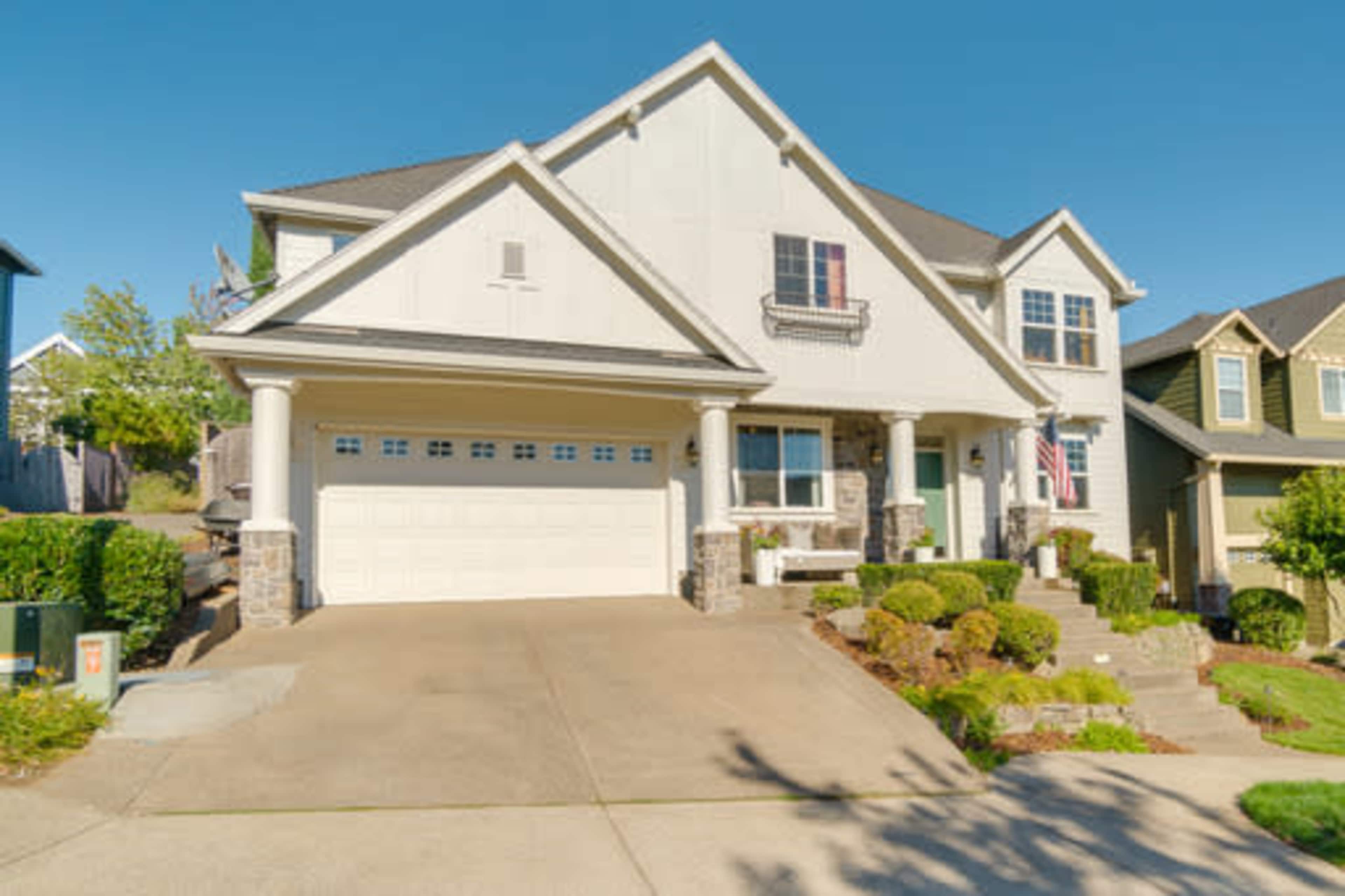 A two-story house with a light-colored exterior, a neatly landscaped yard, and a driveway leading to a three-car garage.