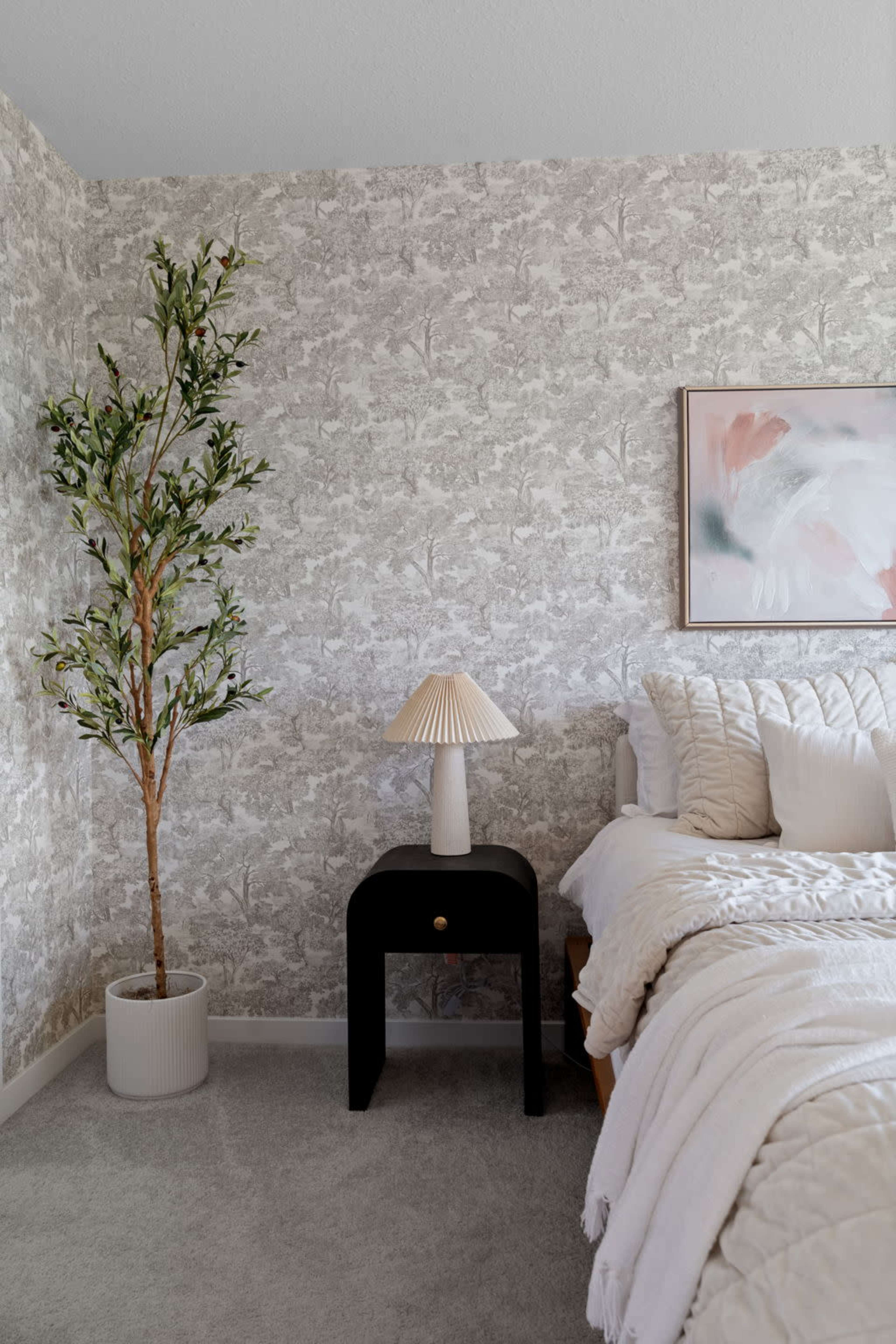 The scene features a cozy bedroom with a patterned wallpaper, a bed with plush bedding, a bedside table with a lamp, and a potted plant.