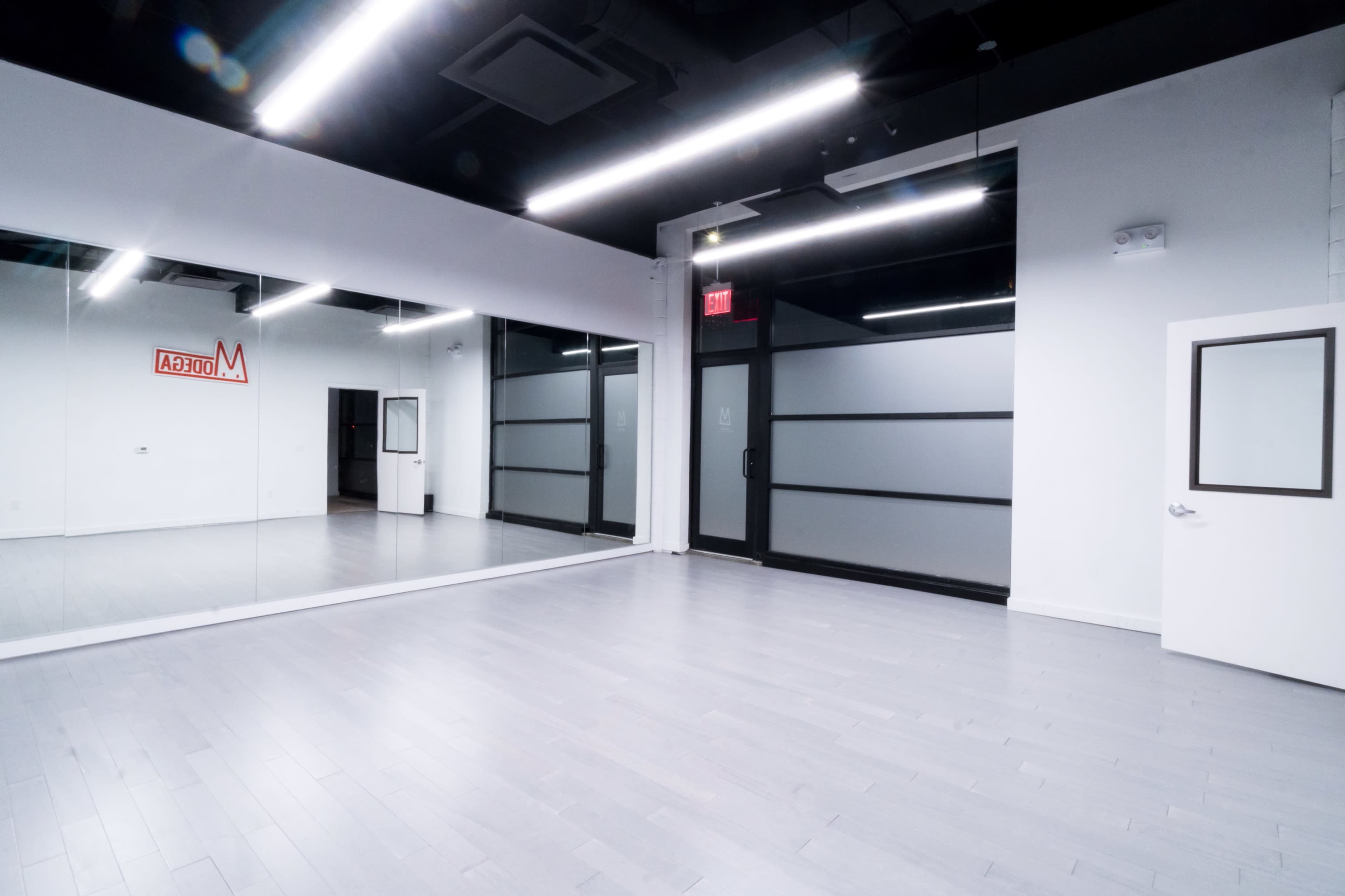 A spacious, minimalistic interior studio with large mirrors, gray flooring, and glass doors.