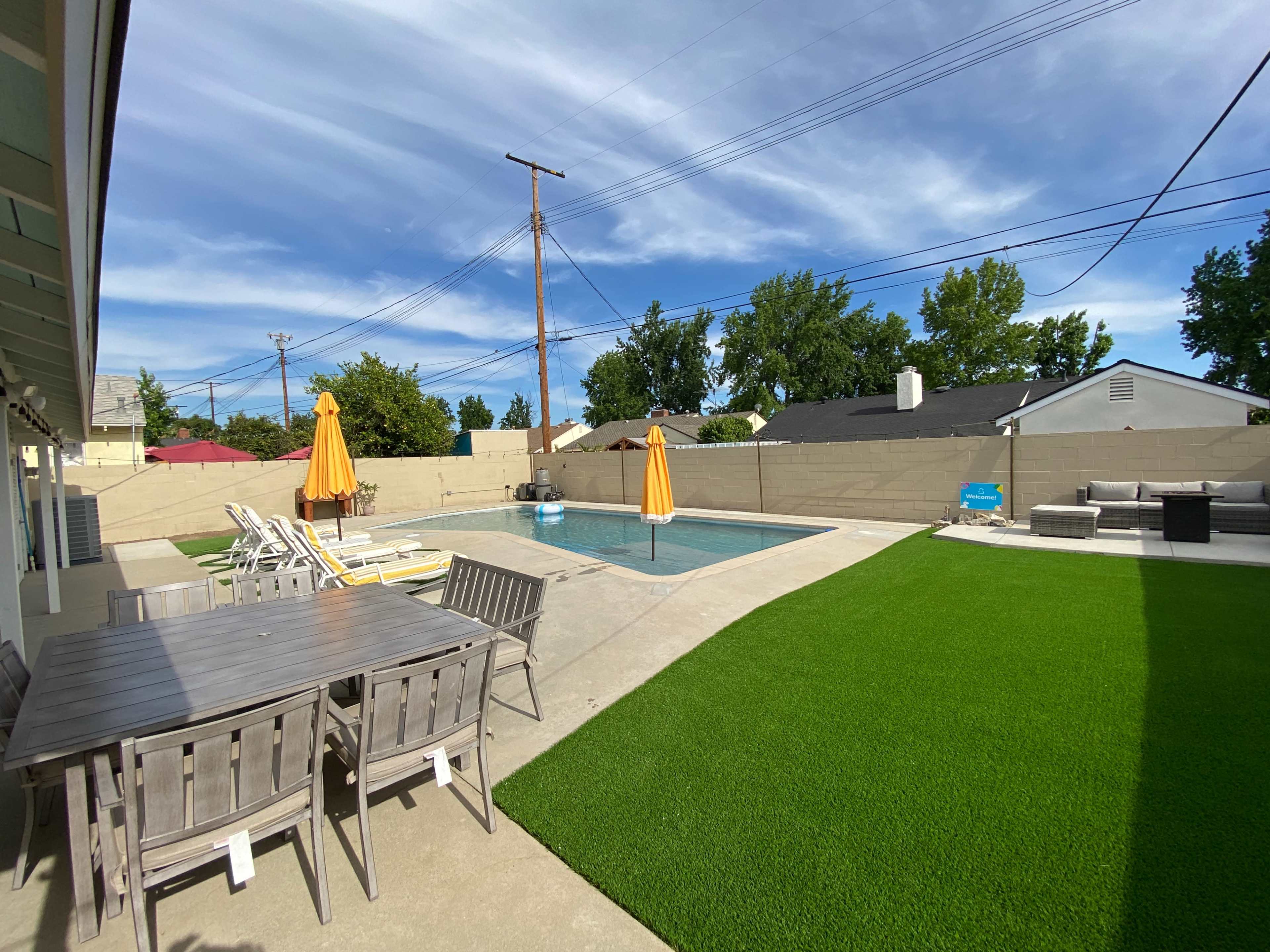A backyard with a swimming pool, patio furniture, and a well-maintained lawn.