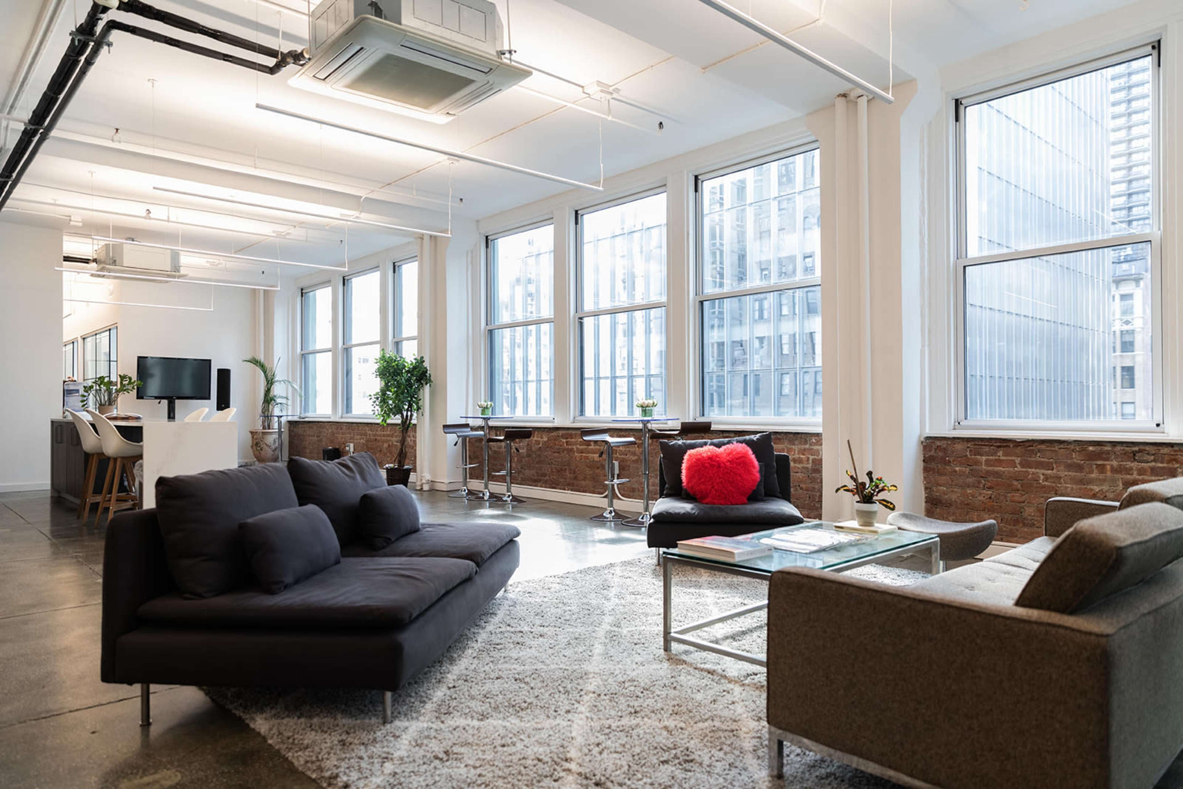 A modern, open-concept office space with large windows, multiple seating areas, and an area rug on the floor.