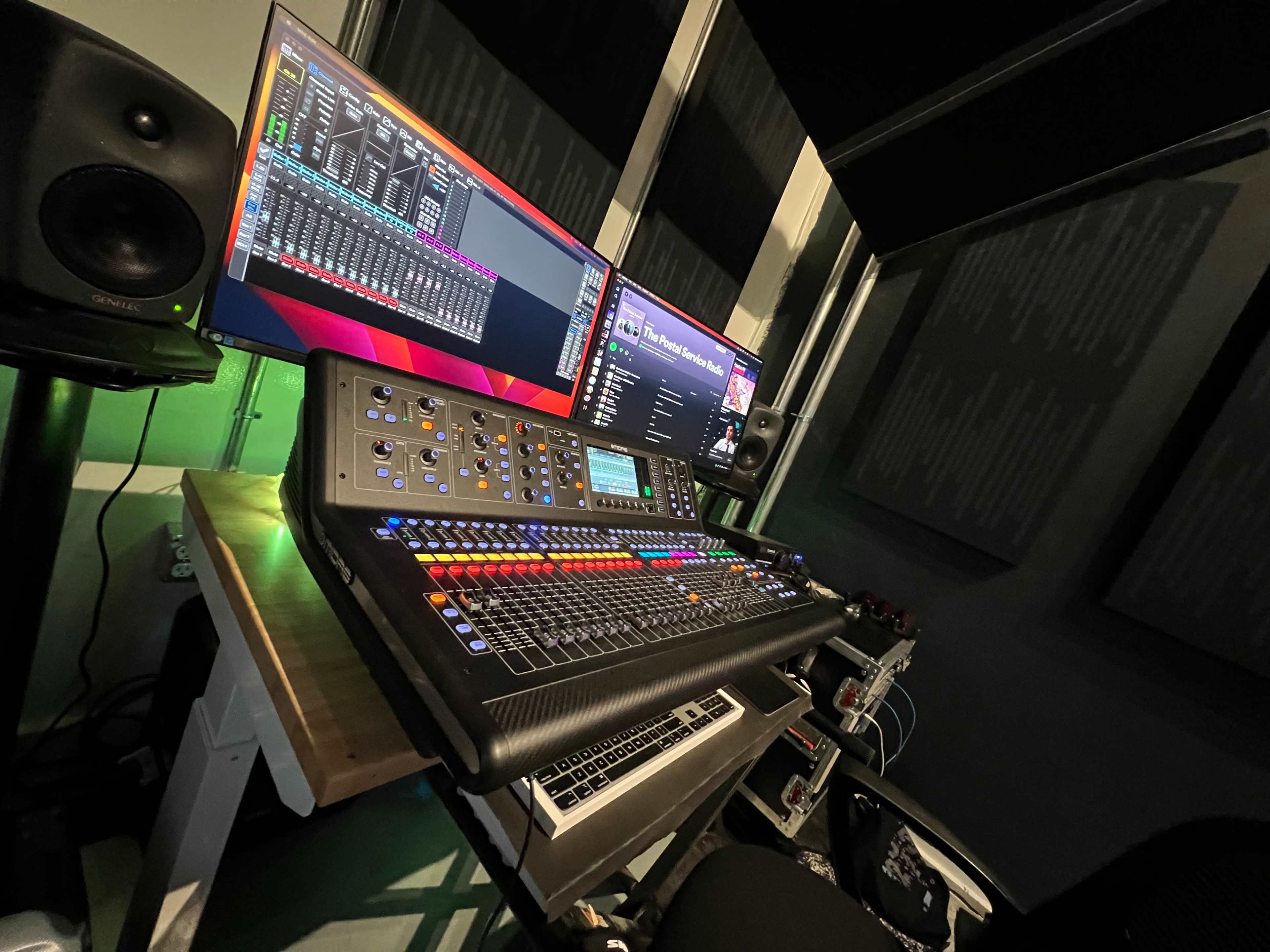 A digital audio mixing console with two connected monitors is set up in a sound recording studio.
