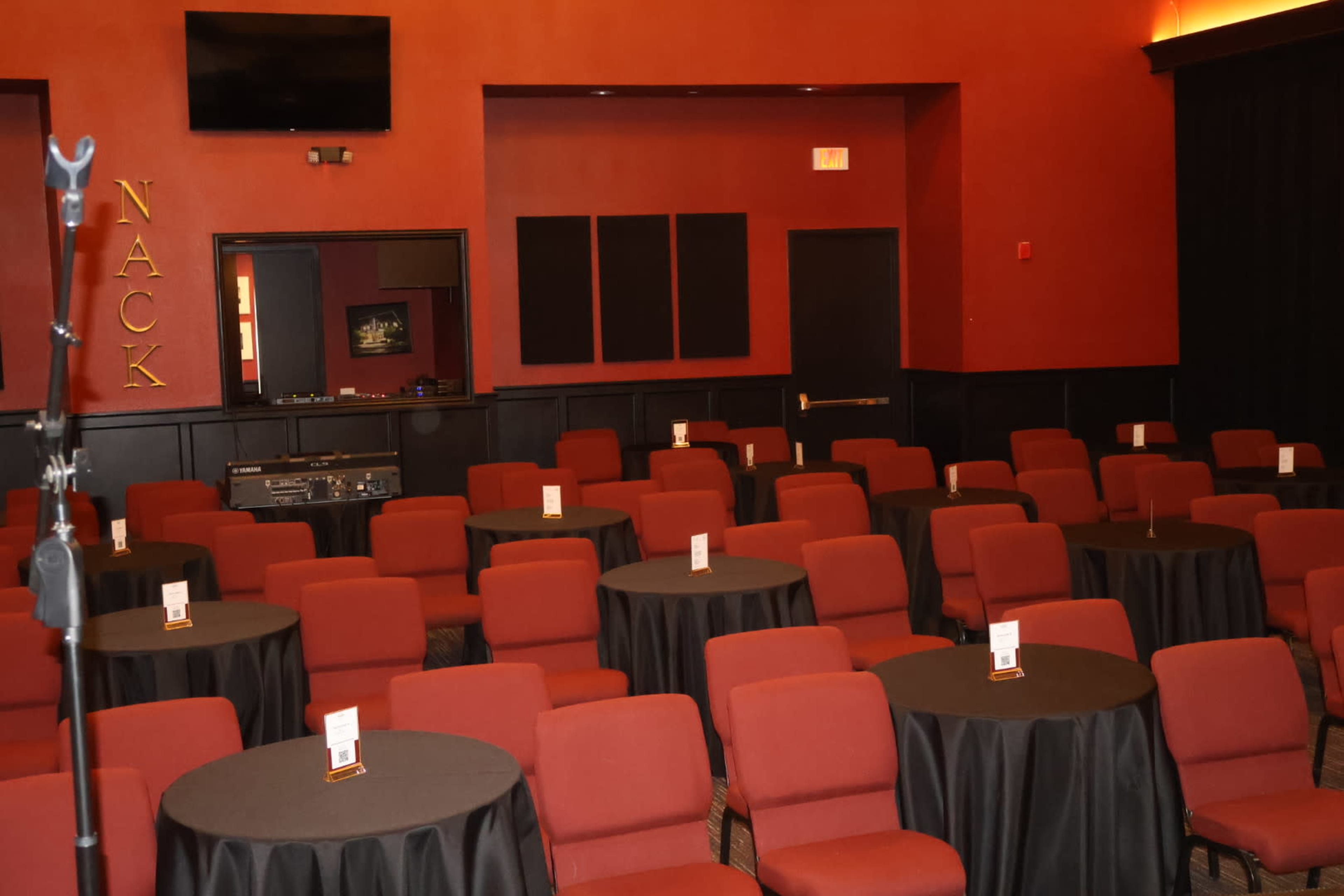 The image shows a conference room set up with rows of red chairs arranged around circular black tables.