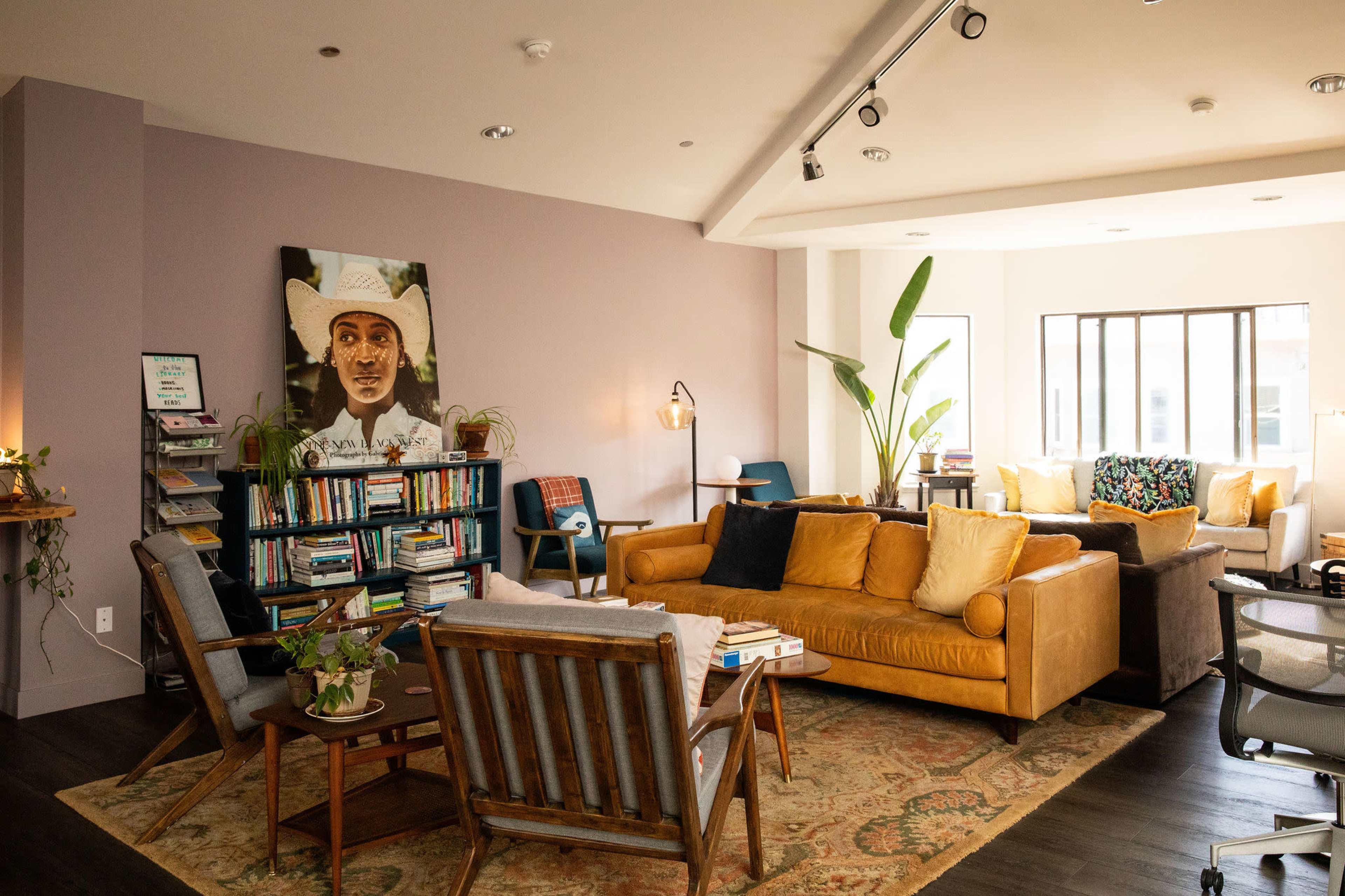 The image shows a cozy living space with a mix of seating options, a bookshelf filled with books, and a large painting of a man on the wall.