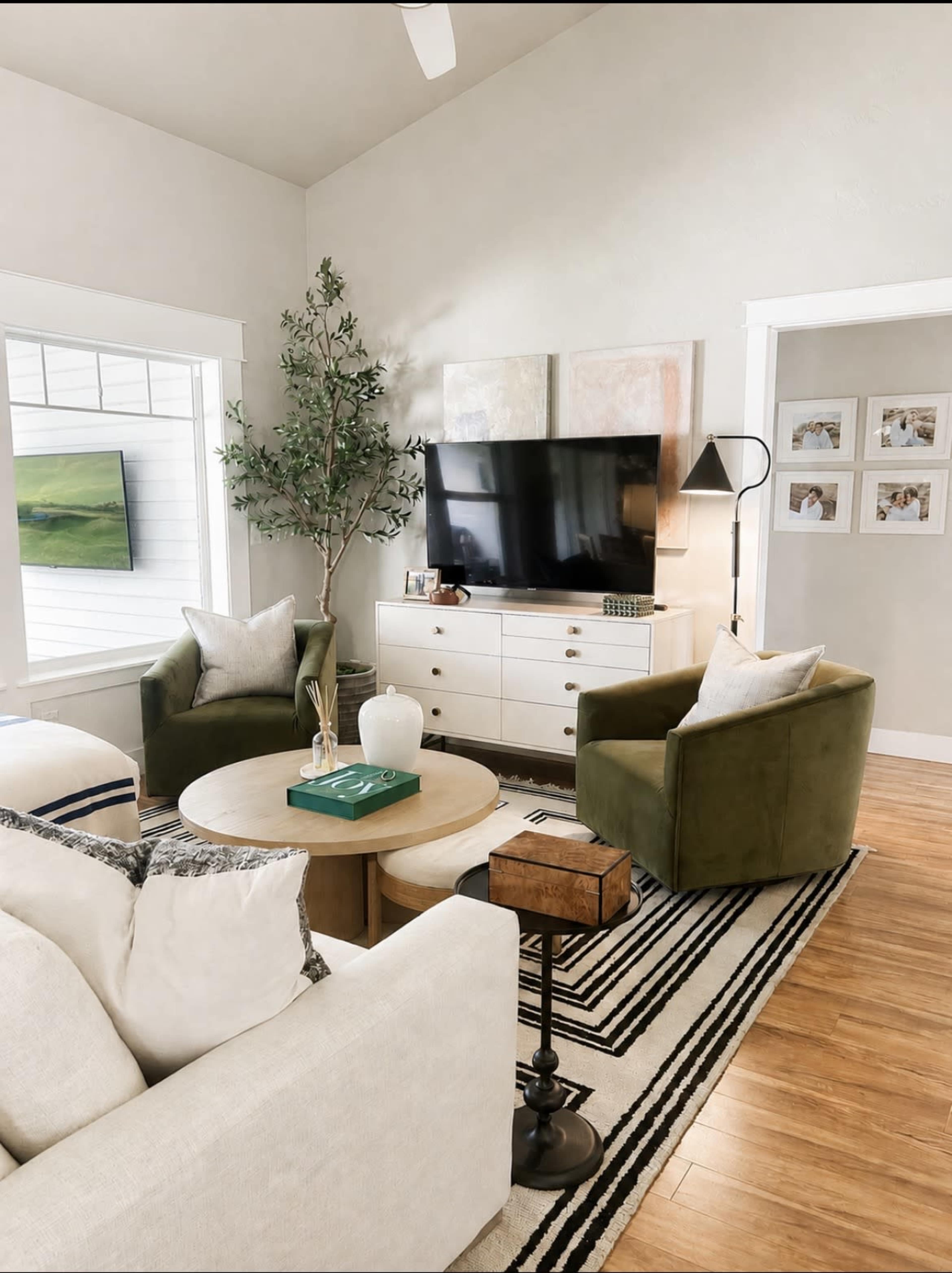 A modern living room features a green armchair, a beige sofa, a round wooden coffee table, and a wall-mounted television.