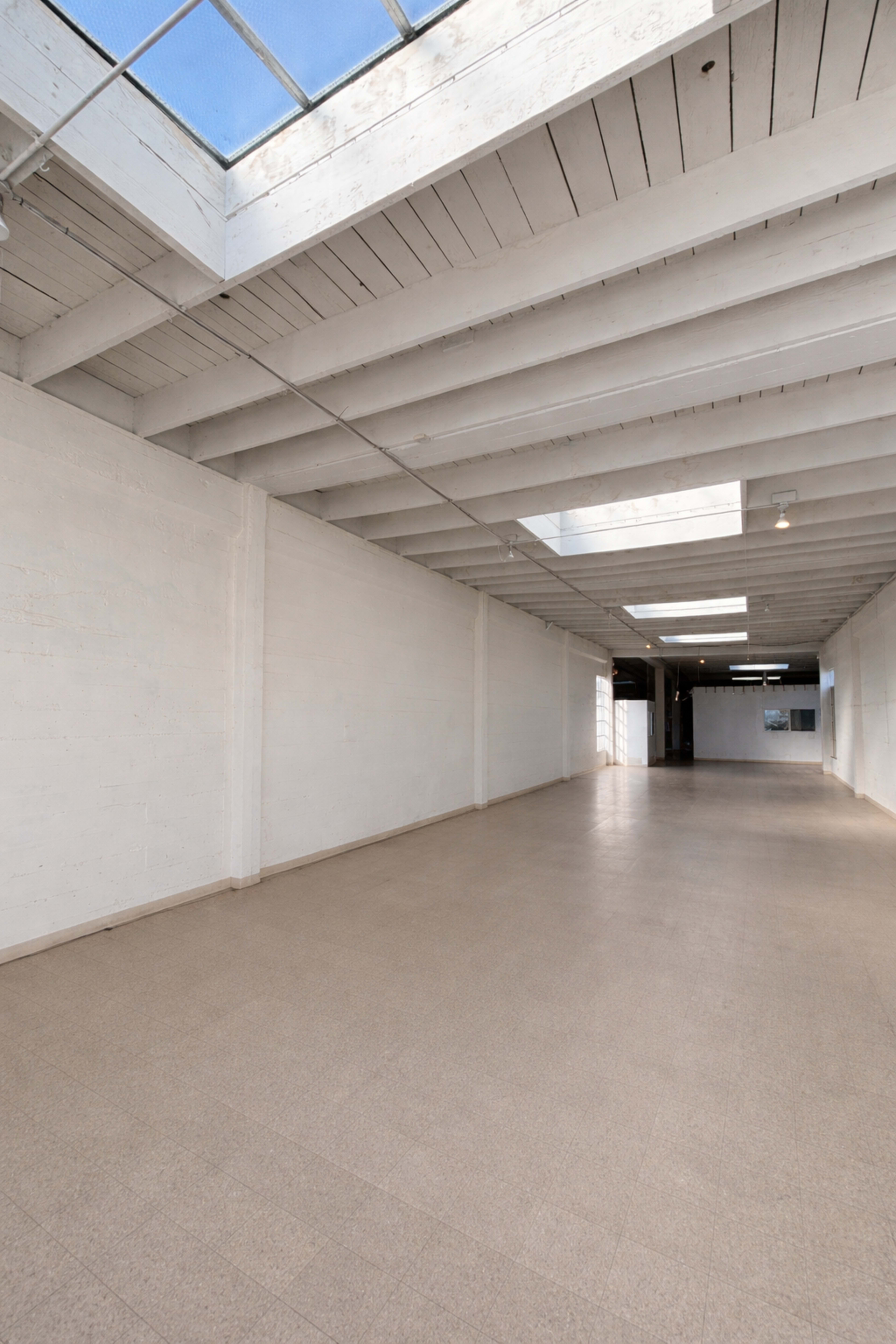 The image shows a spacious, empty room with white walls, a light-colored floor, and a skylight overhead.