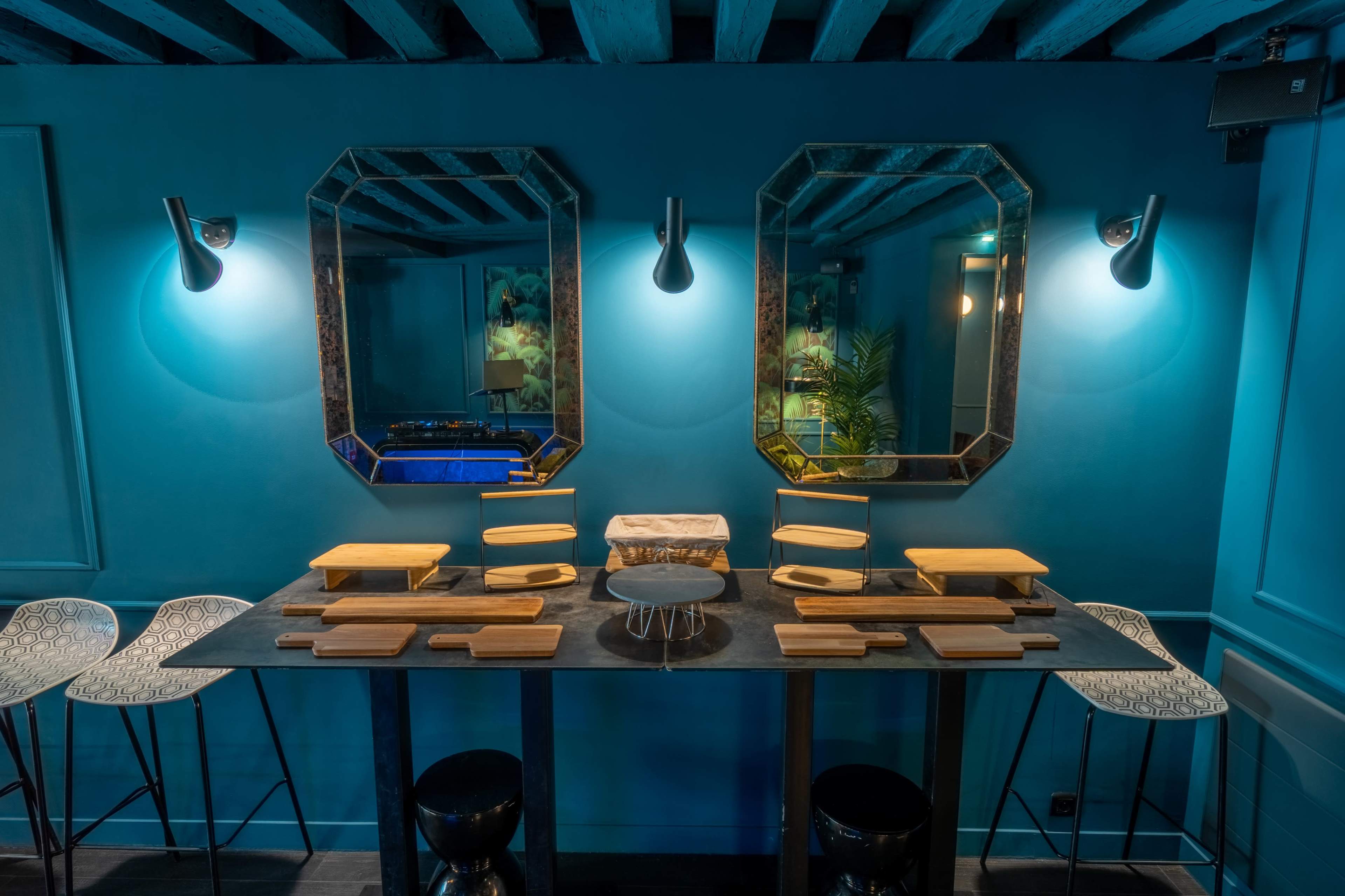 A modern dining area with a blue wall, two ornate mirrors, and a long table set with multiple wooden platters.