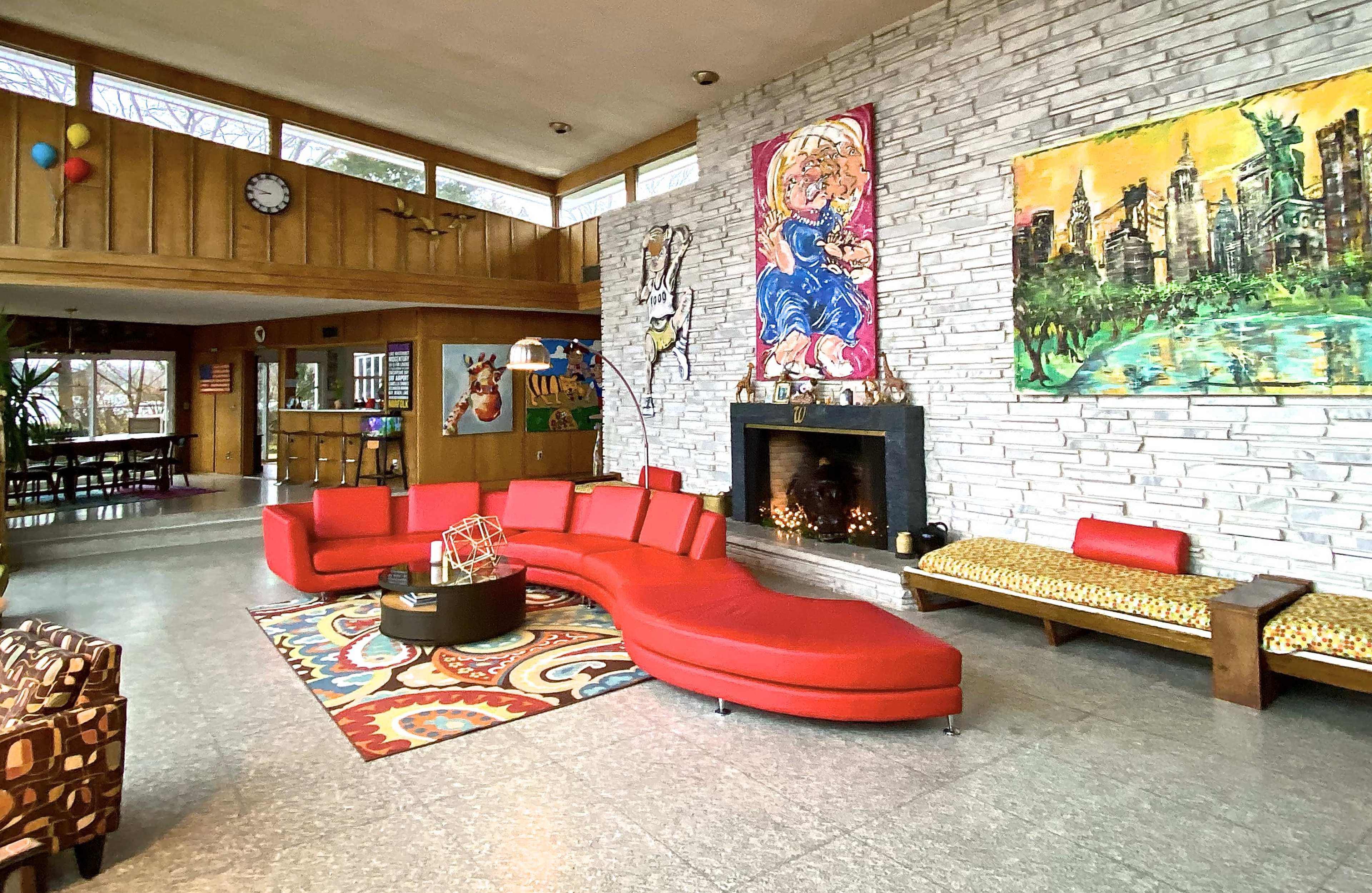 A spacious living room with a vibrant red curved sofa, a fireplace, and colorful artwork on the stone wall.