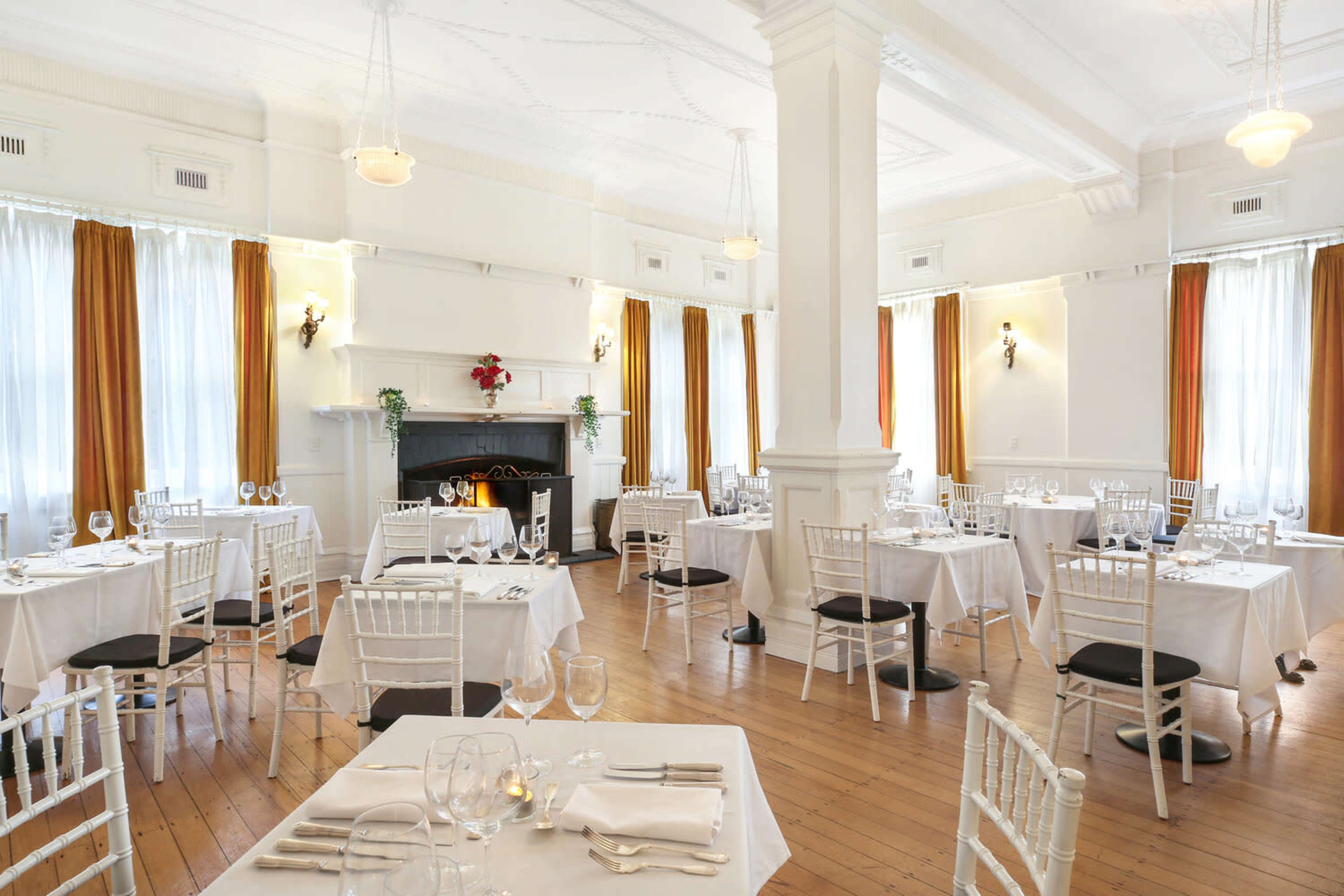 A well-lit restaurant featuring neatly arranged tables with white tablecloths, surrounded by large windows adorned with orange curtains.