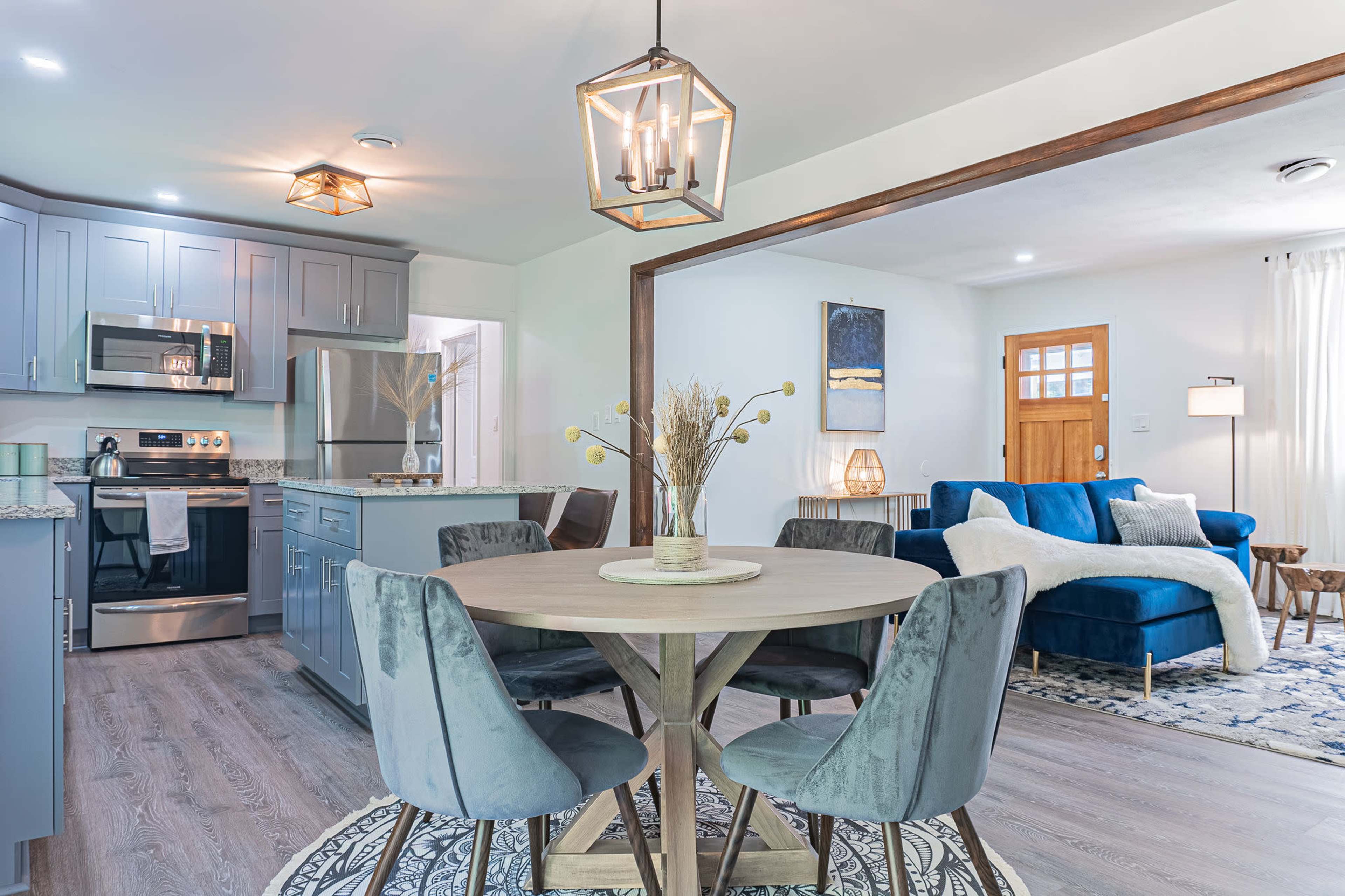 A modern kitchen connected to a dining area, featuring a round table with four chairs and a cozy living room in the background.