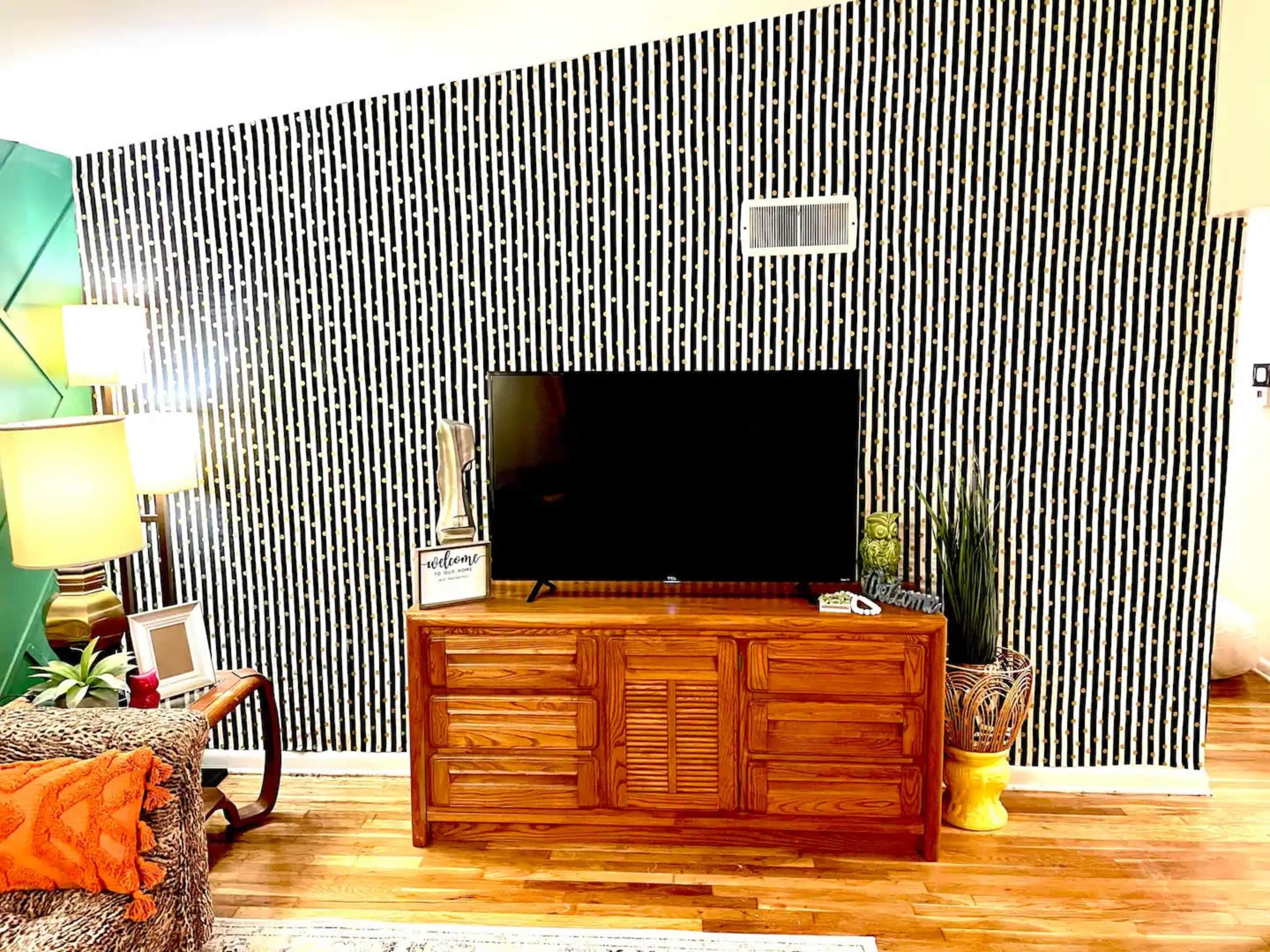 A living room with a wooden television stand, a black-screened TV, and a patterned accent wall covered in vertical stripes.