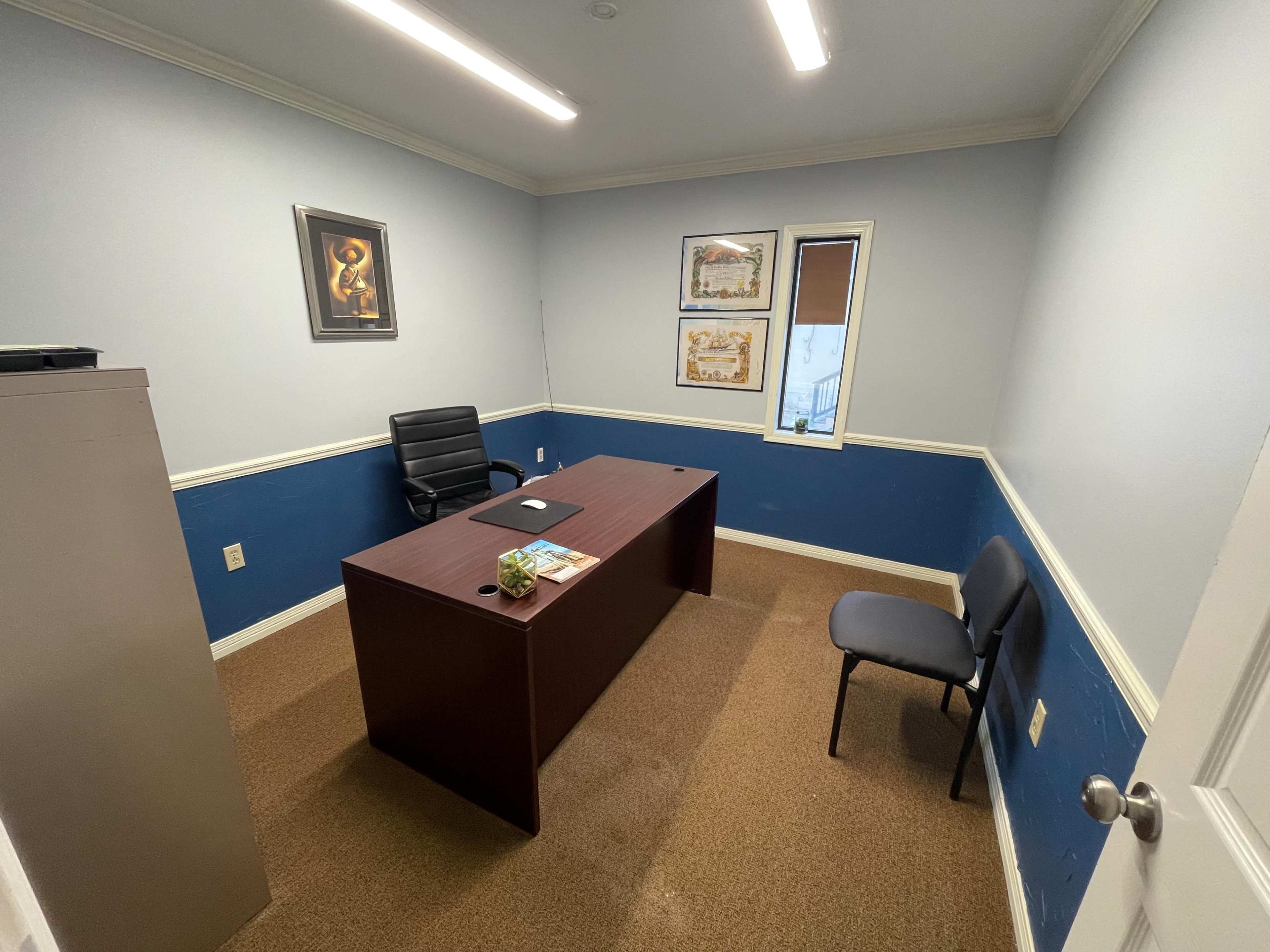 The image shows a small office space with a desk, a chair, and a filing cabinet against the walls painted in blue, and a window on one side.