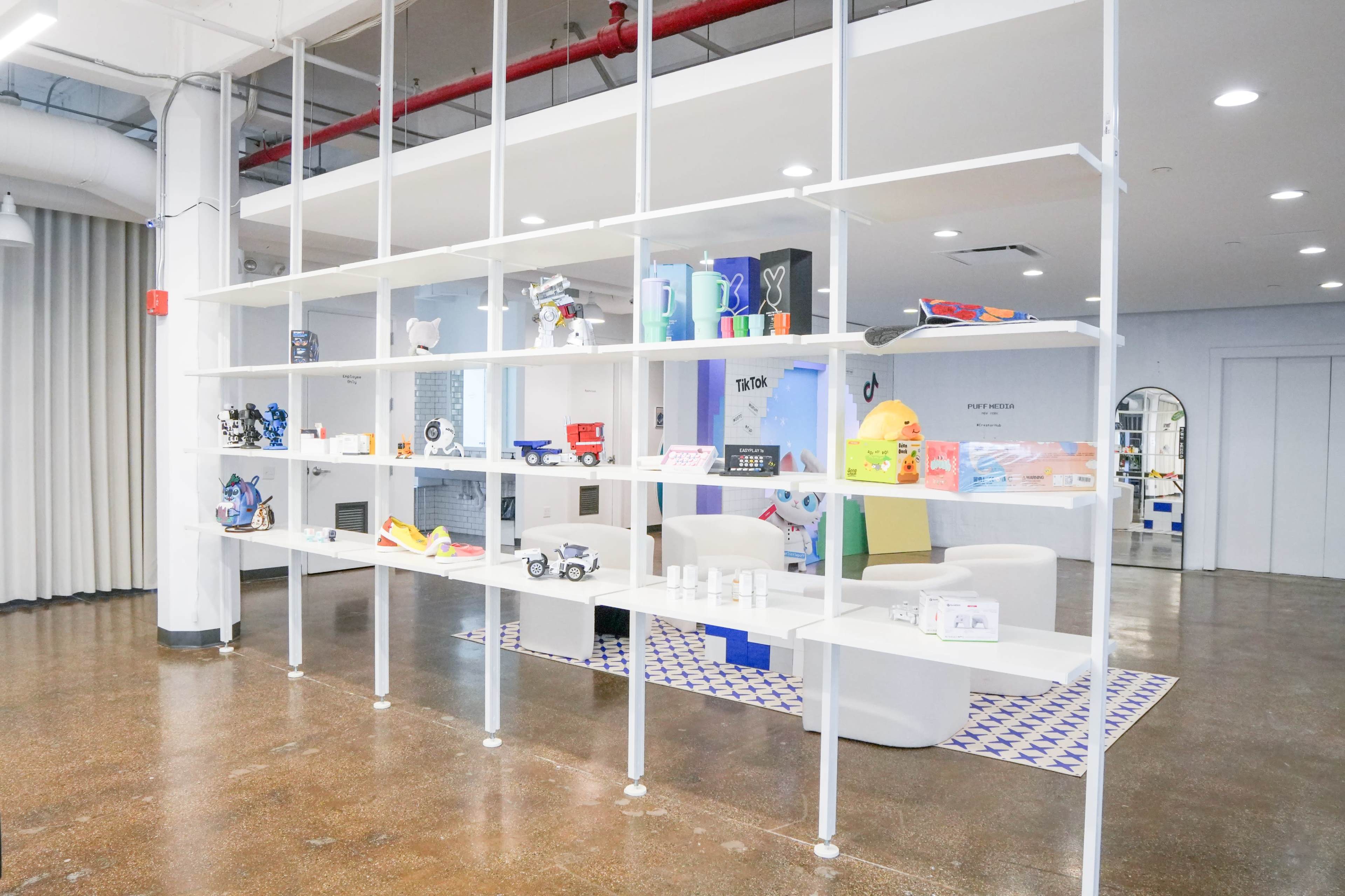 The image shows a modern display shelf with a variety of colorful toys and gadgets arranged neatly on its white surfaces in a well-lit space.