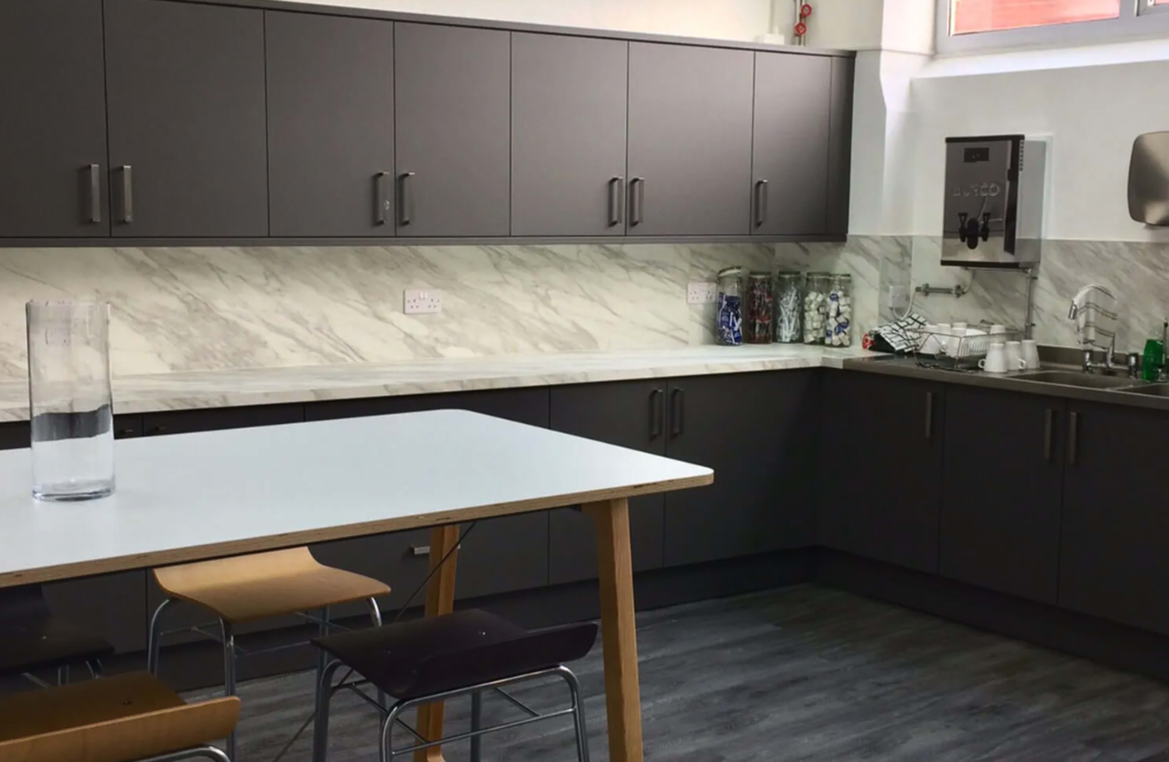 The image shows a modern kitchen with gray cabinets, a white marble backsplash, a wooden table, and several chairs.