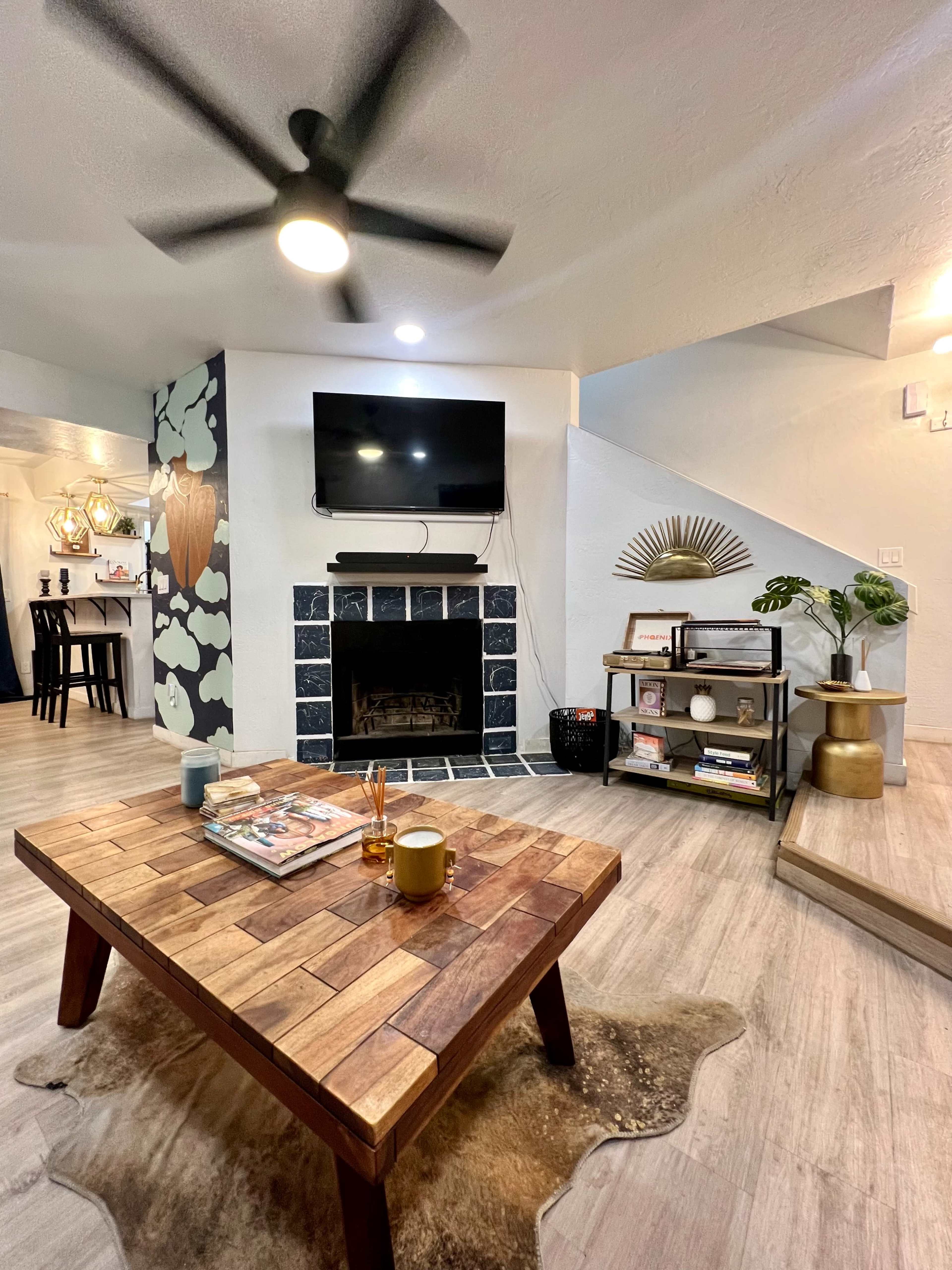 A modern living room featuring a wooden coffee table, a fireplace with a television above it, and a decorative staircase in the background.