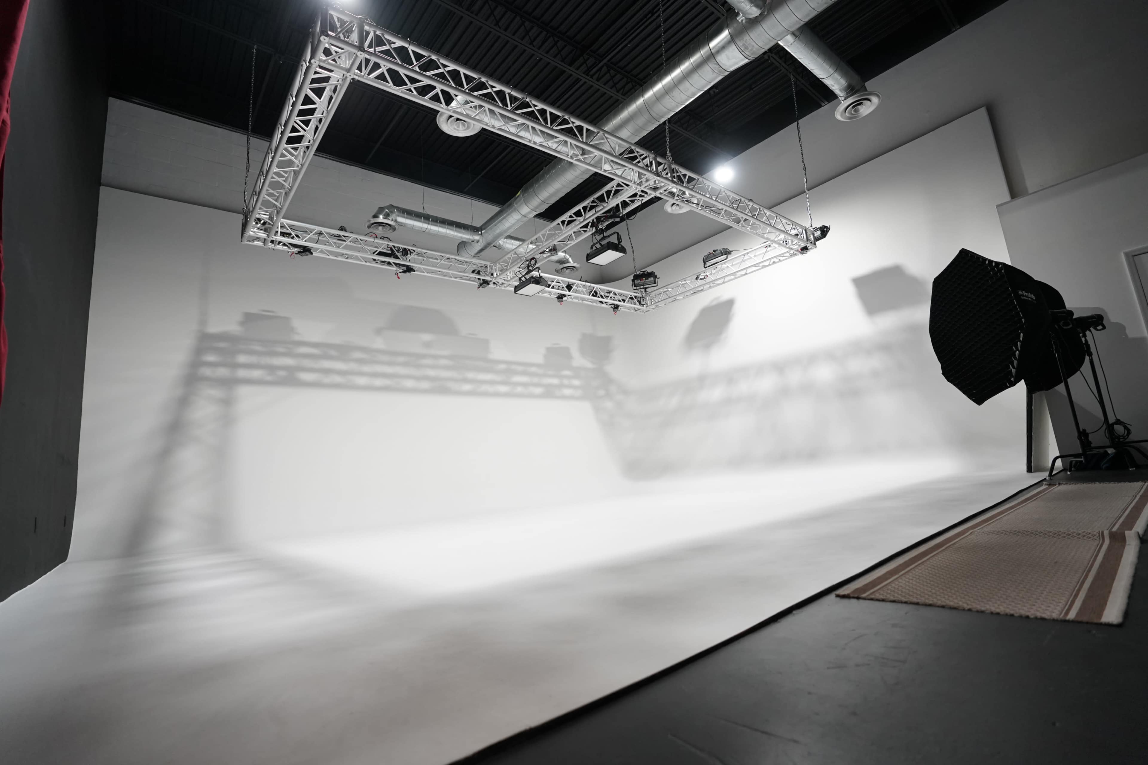 The image shows a spacious, well-lit photography studio with a white backdrop and overhead lighting equipment.