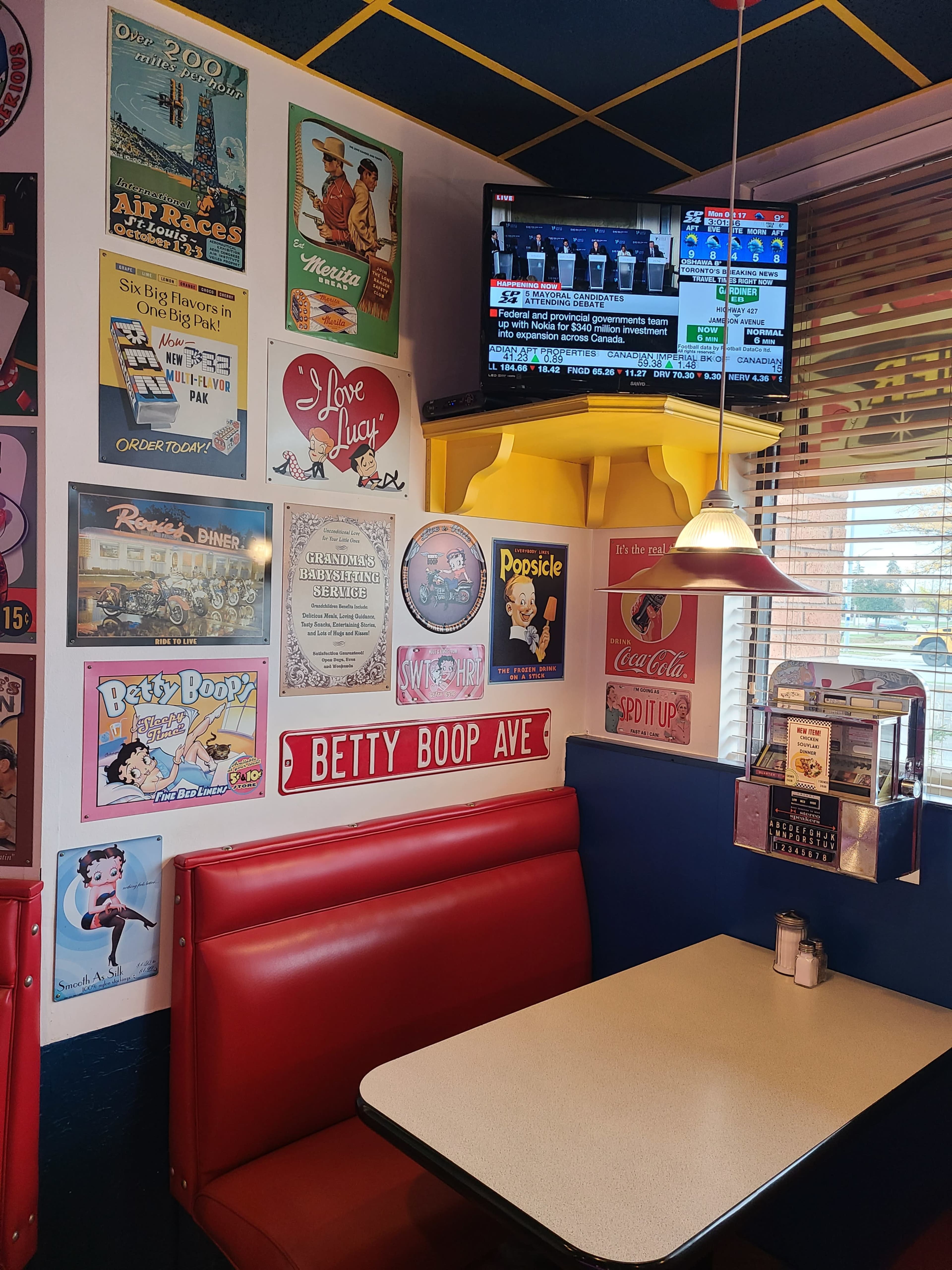 A corner booth in a diner features colorful vintage advertisements and a TV mounted on the wall displaying news.