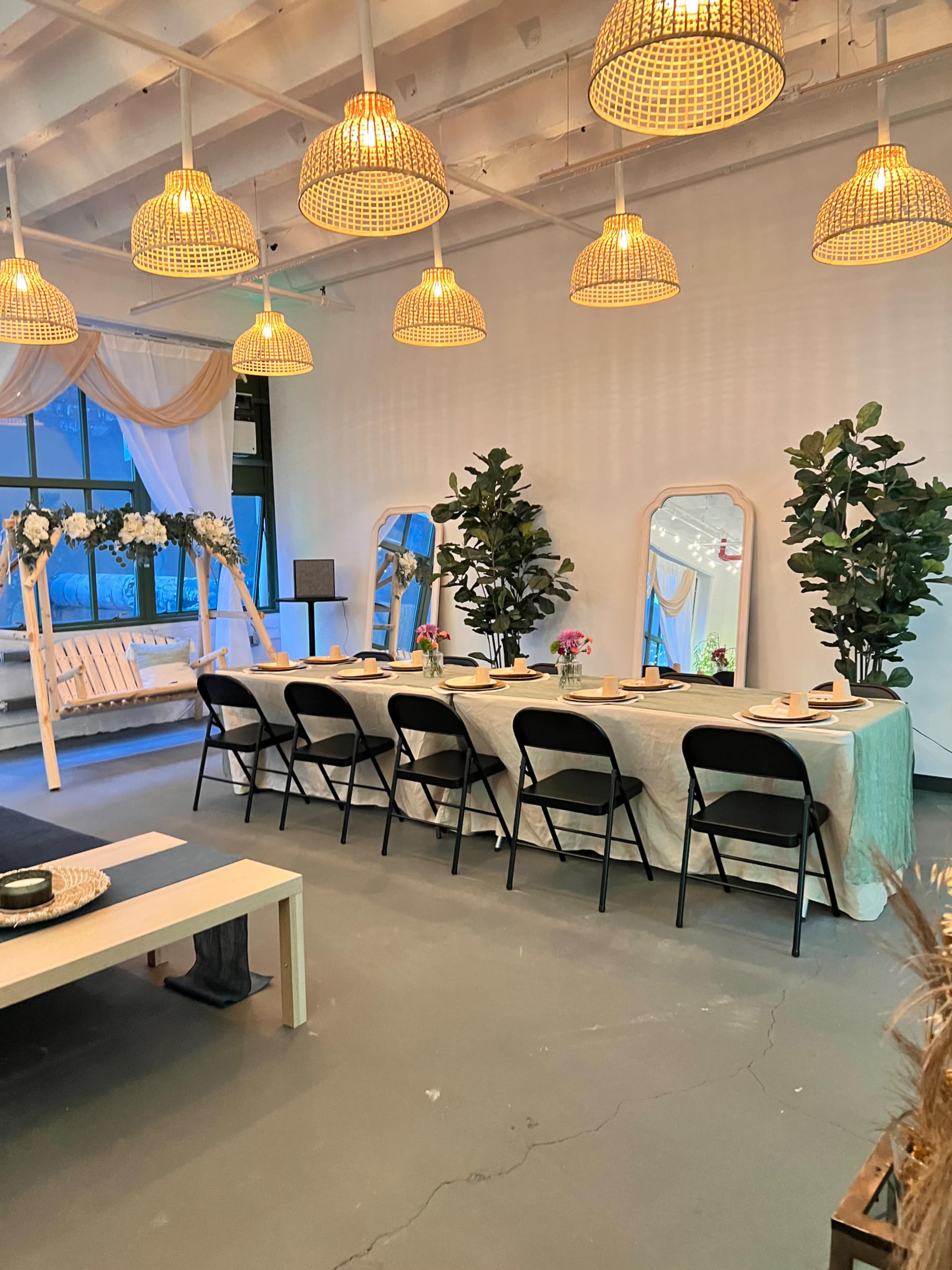 A long table is set for an event in a modern space with decorative plants and hanging light fixtures.