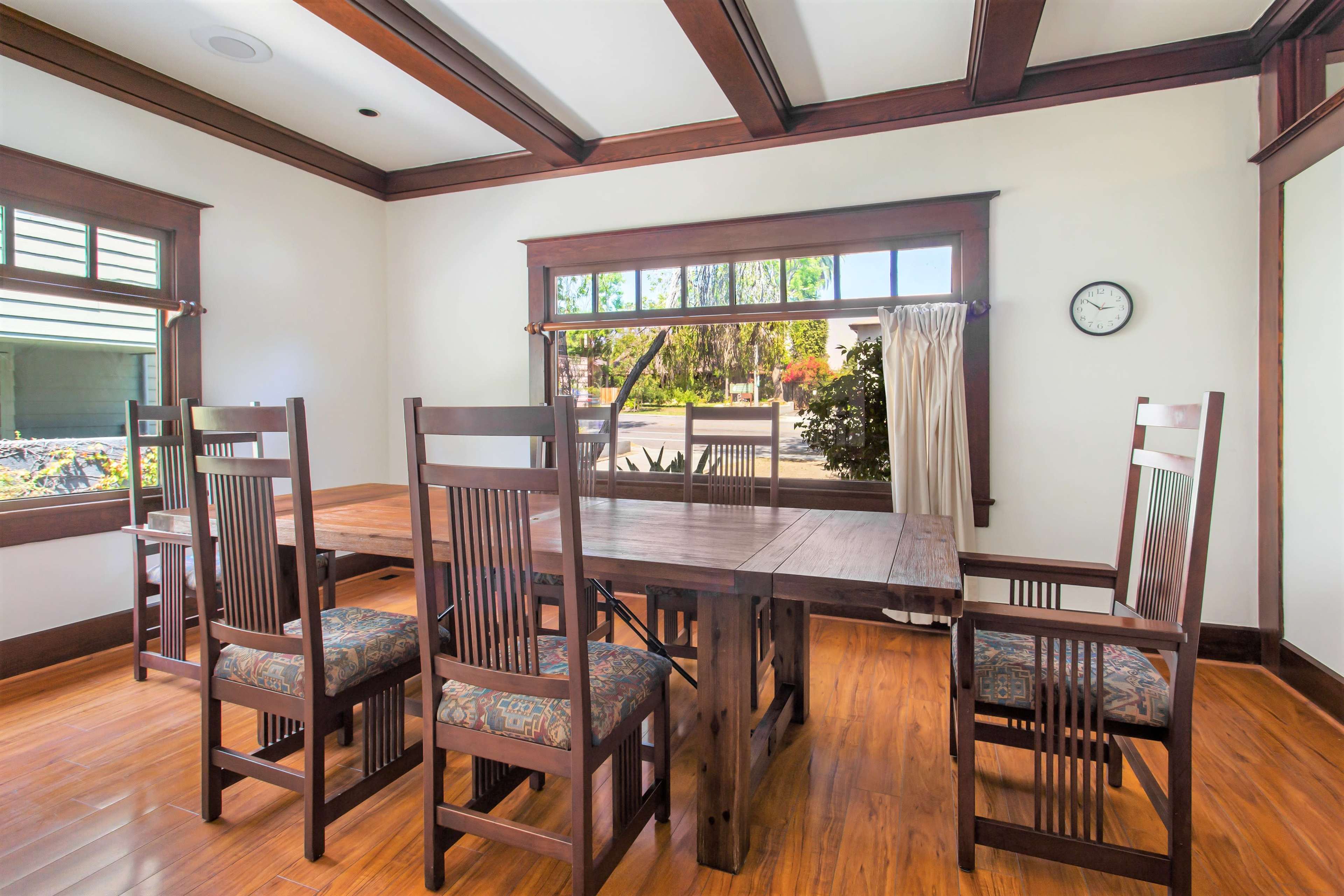 A spacious dining room features a wooden table surrounded by six chairs, with large windows allowing natural light to enter.