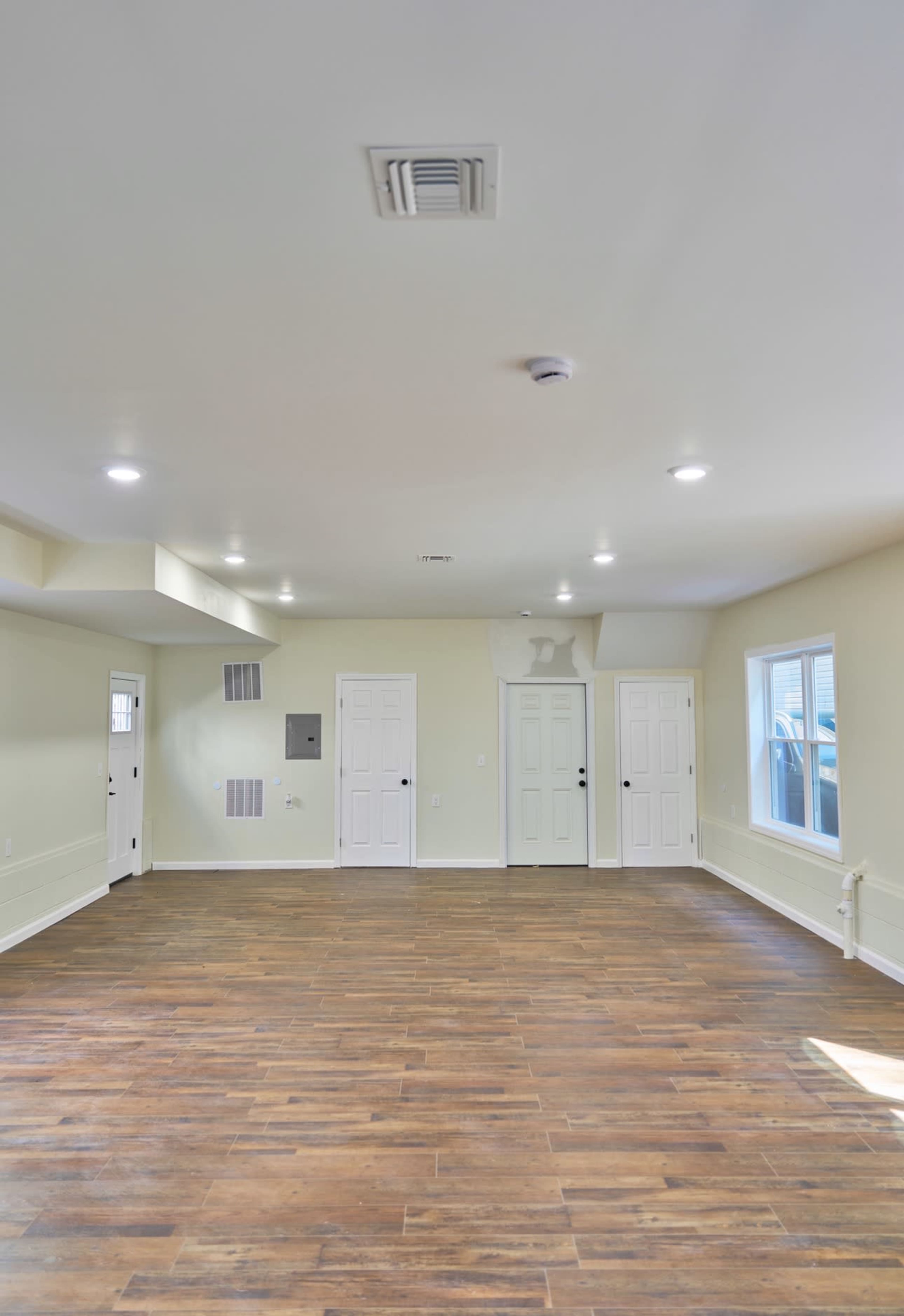 The image shows an empty room with brown wooden flooring, light walls, and multiple doors.