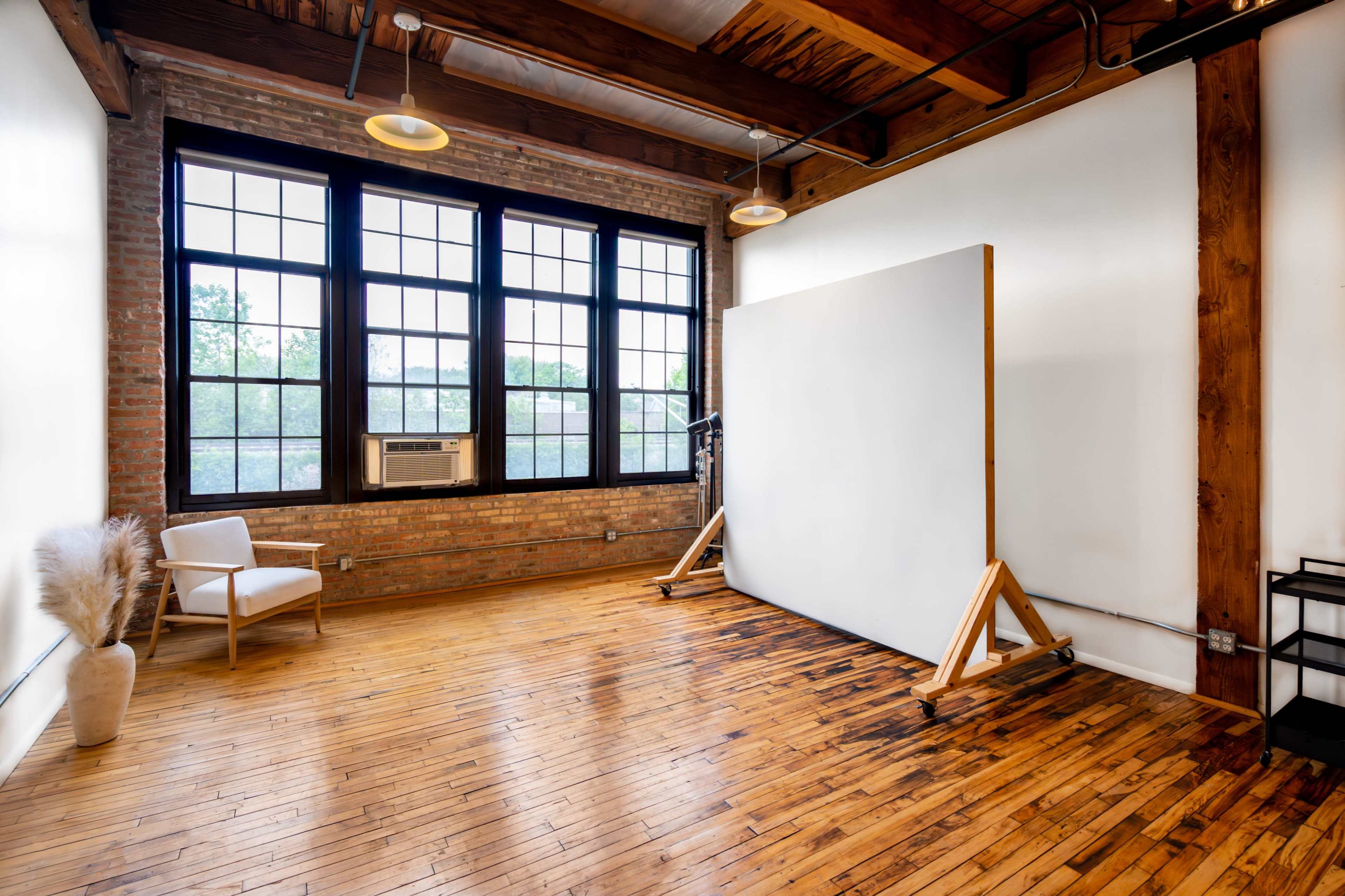 A minimalistic studio space with large windows, hardwood floors, and a blank canvas positioned on a wooden easel.