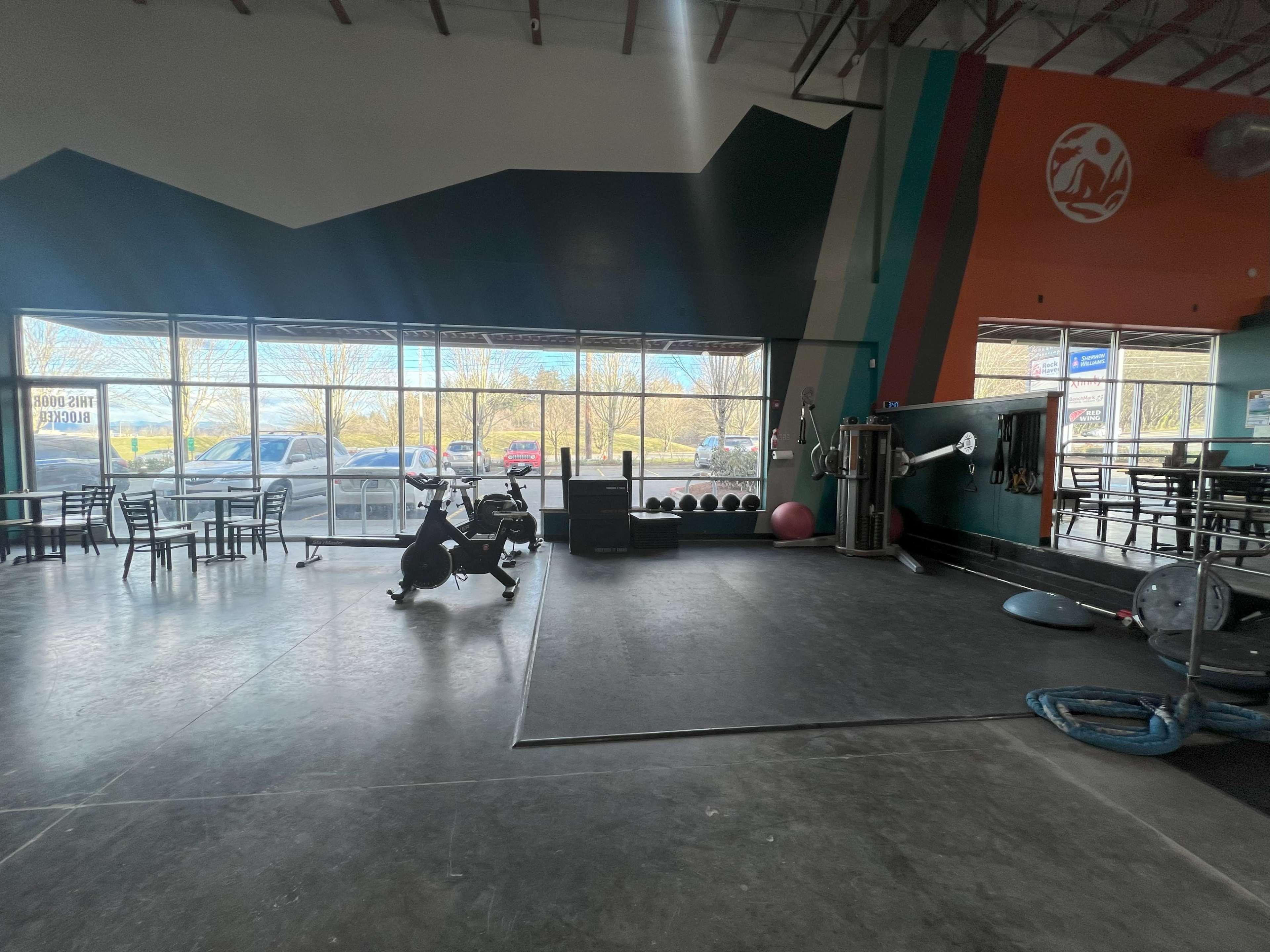 An indoor gym with exercise equipment, large windows on one side, and a section for weights and fitness mats.