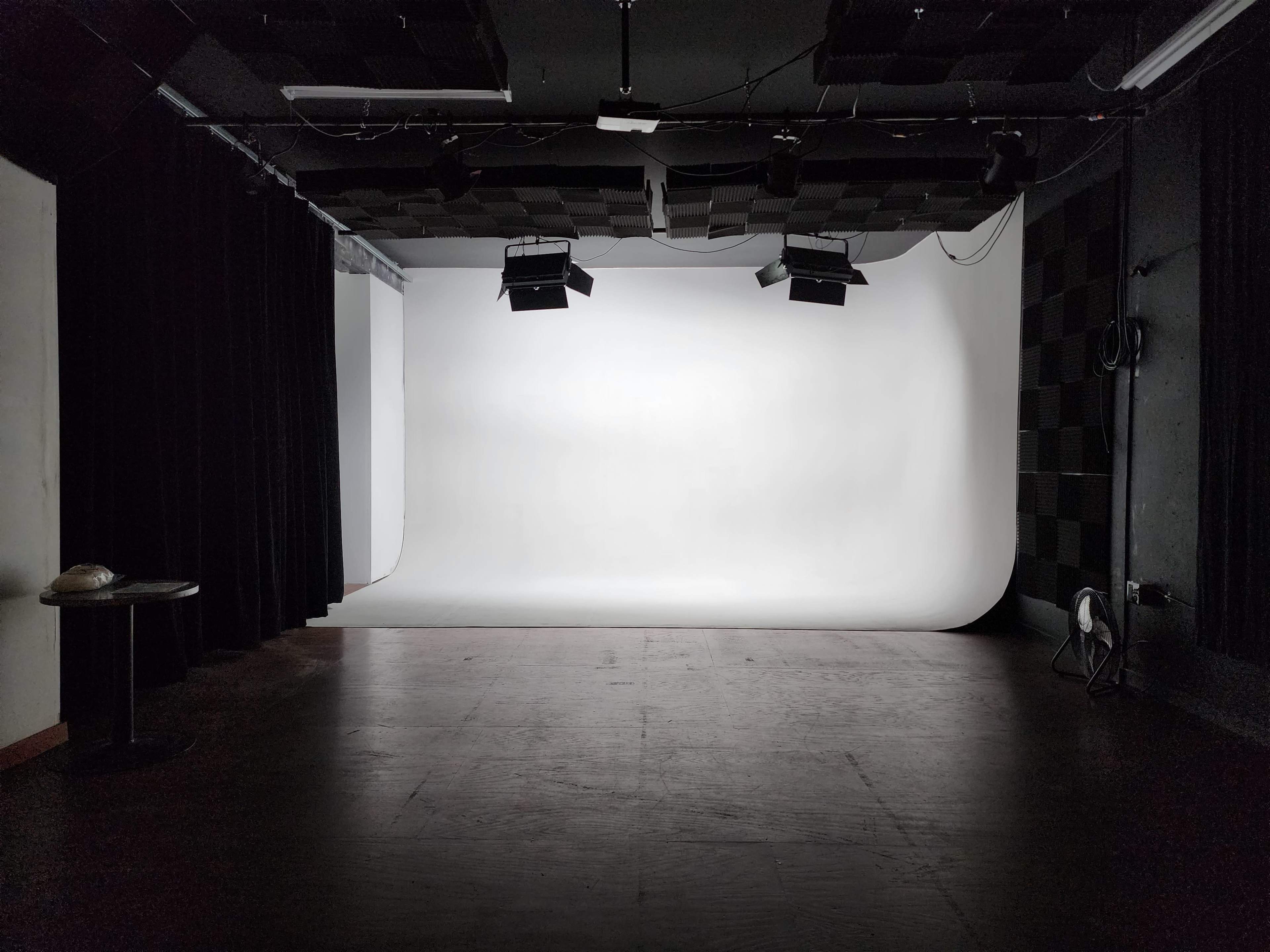 A dimly lit photography studio with a seamless white backdrop and two overhead lights.