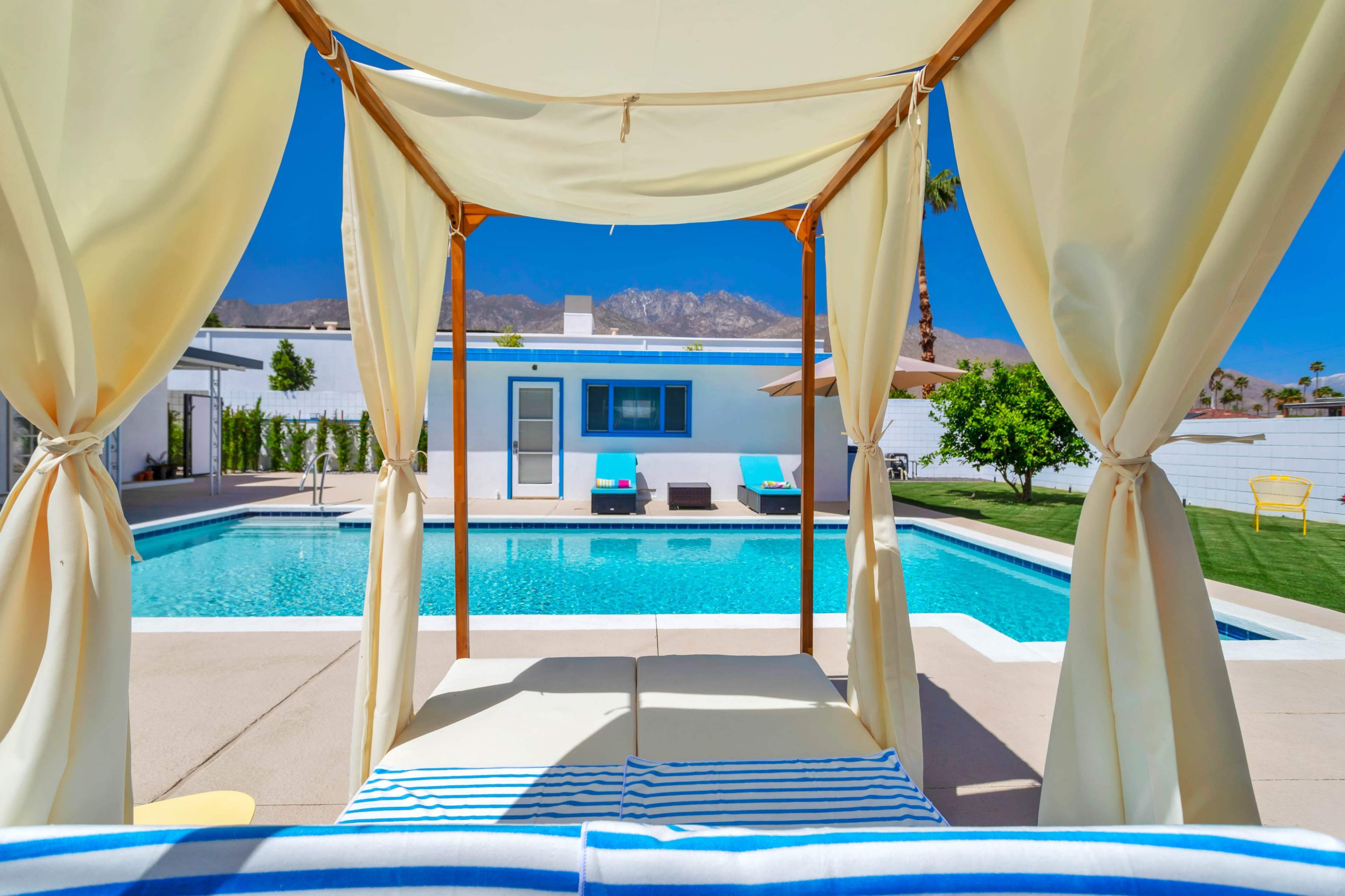 A pool area with a cabana overlooking a turquoise swimming pool surrounded by lounge chairs and a backdrop of mountains.