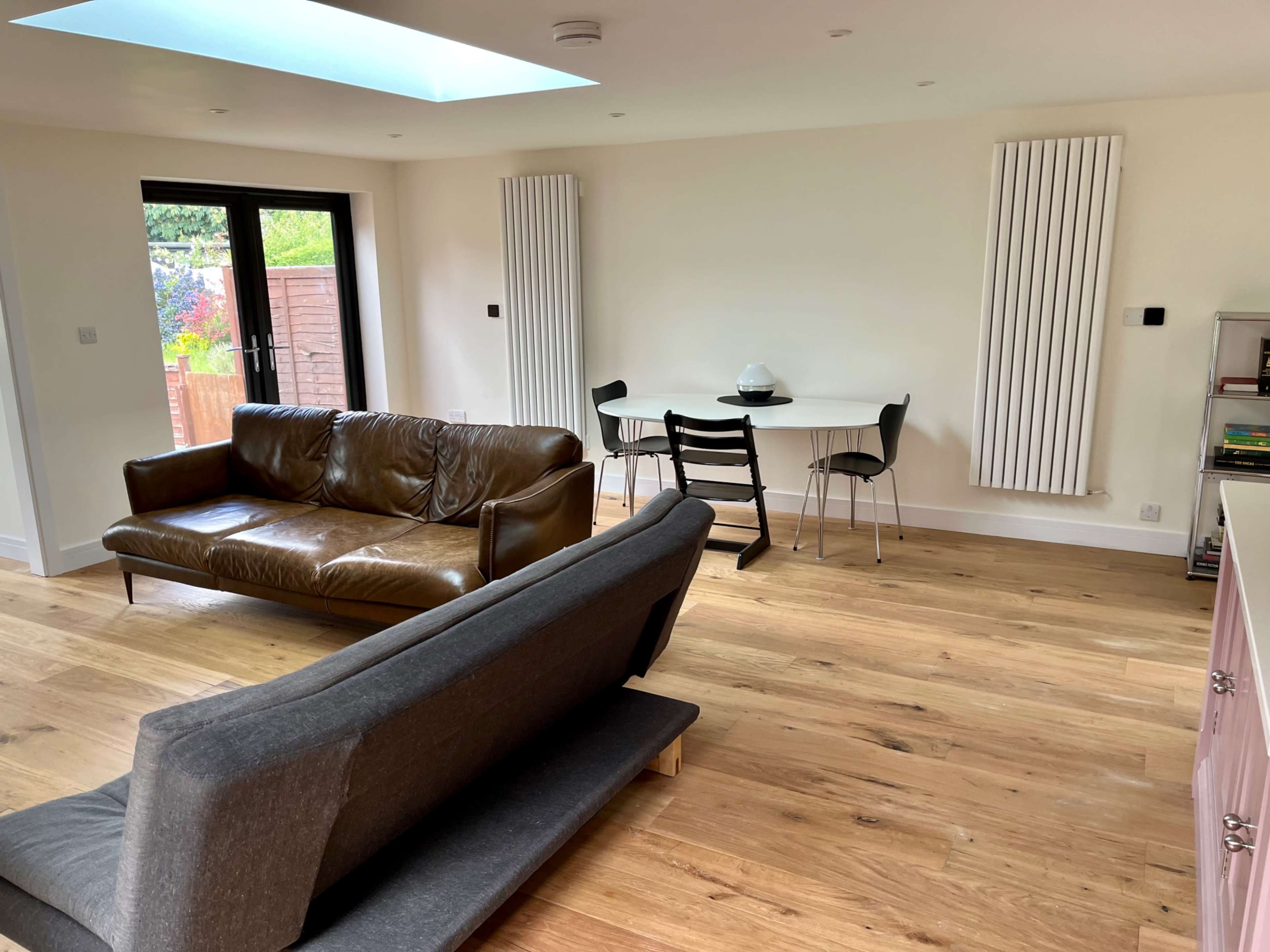 A modern living space with a brown leather sofa, a gray couch, a circular dining table with black chairs, and wooden flooring.