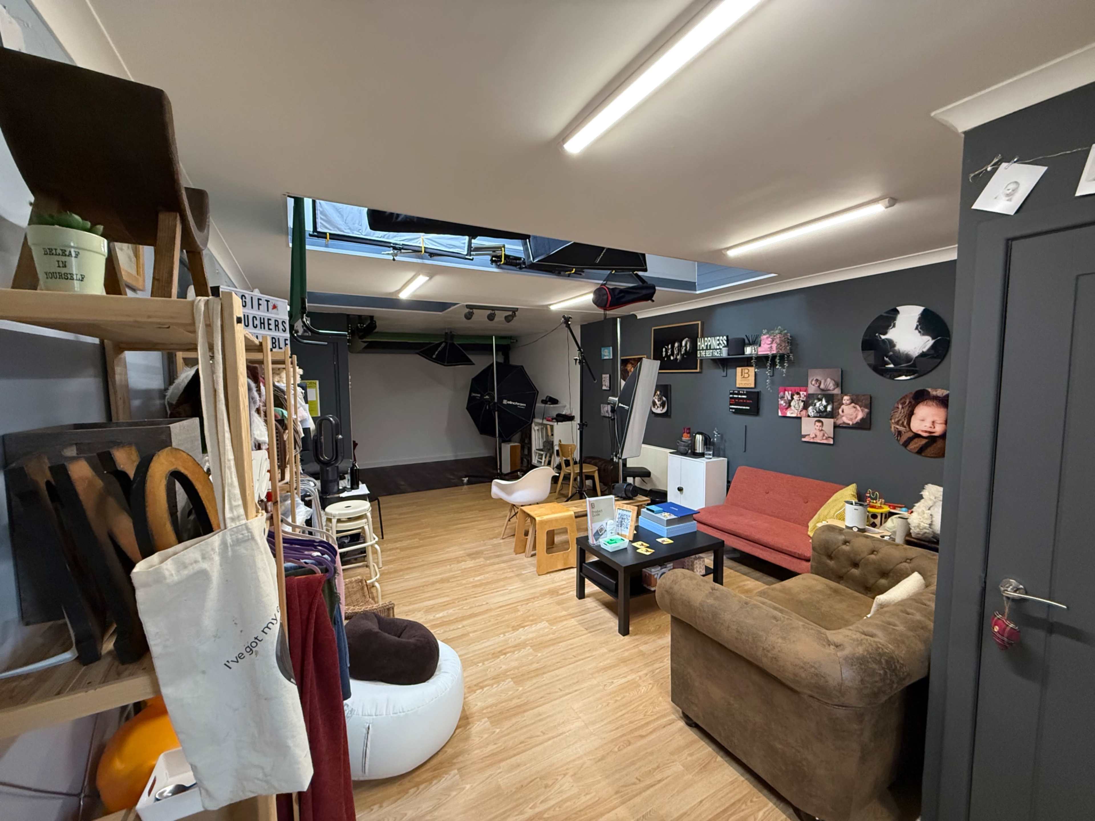 The image shows a well-lit studio space with various seating options, a wooden floor, and photography equipment in the background.