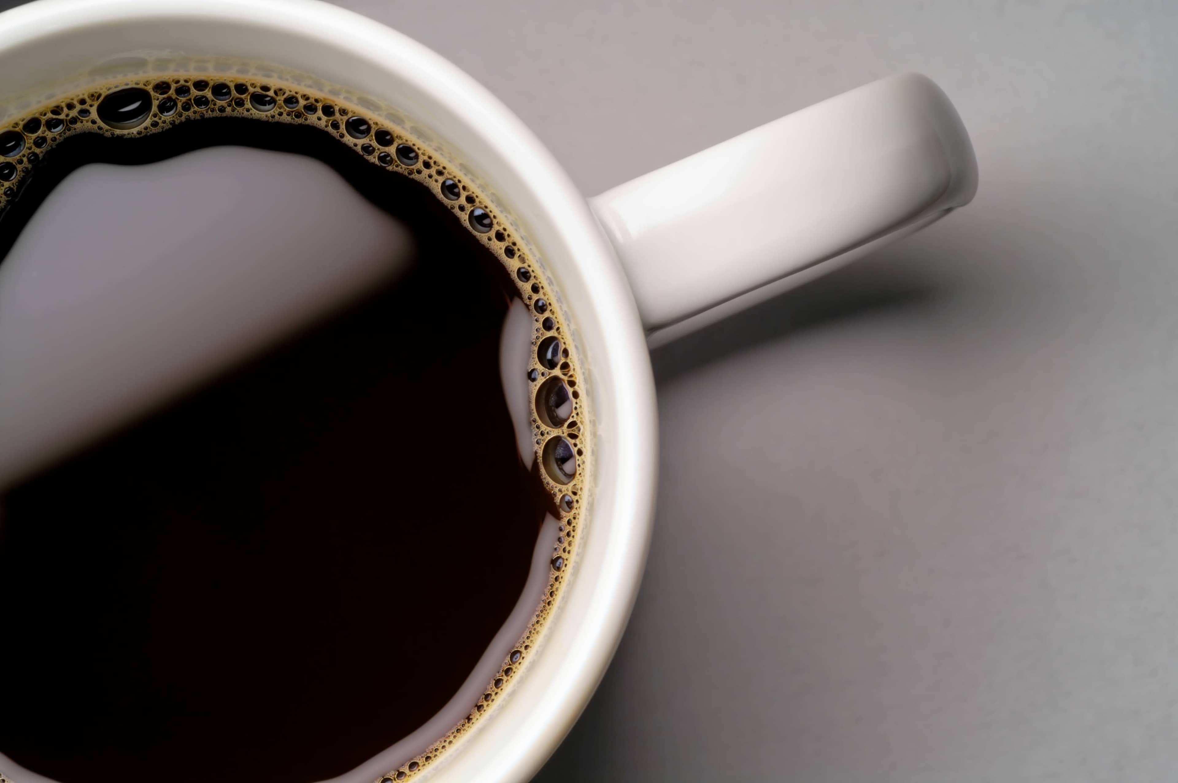 A close-up view of a white coffee mug filled with black coffee, showing bubbles along the rim.