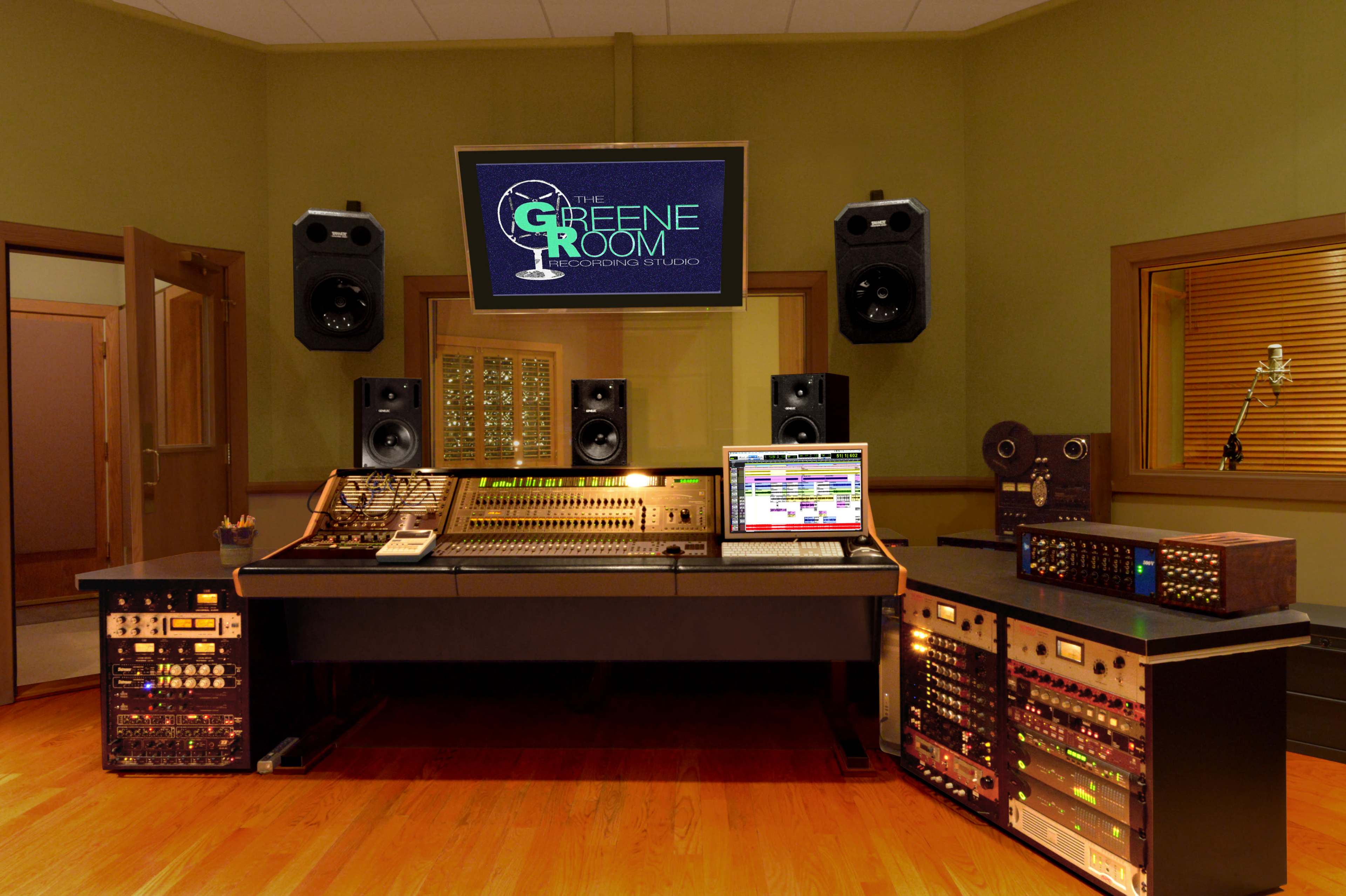 A recording studio with a central mixing console, a computer displaying audio software, and multiple speakers and racks of audio equipment.