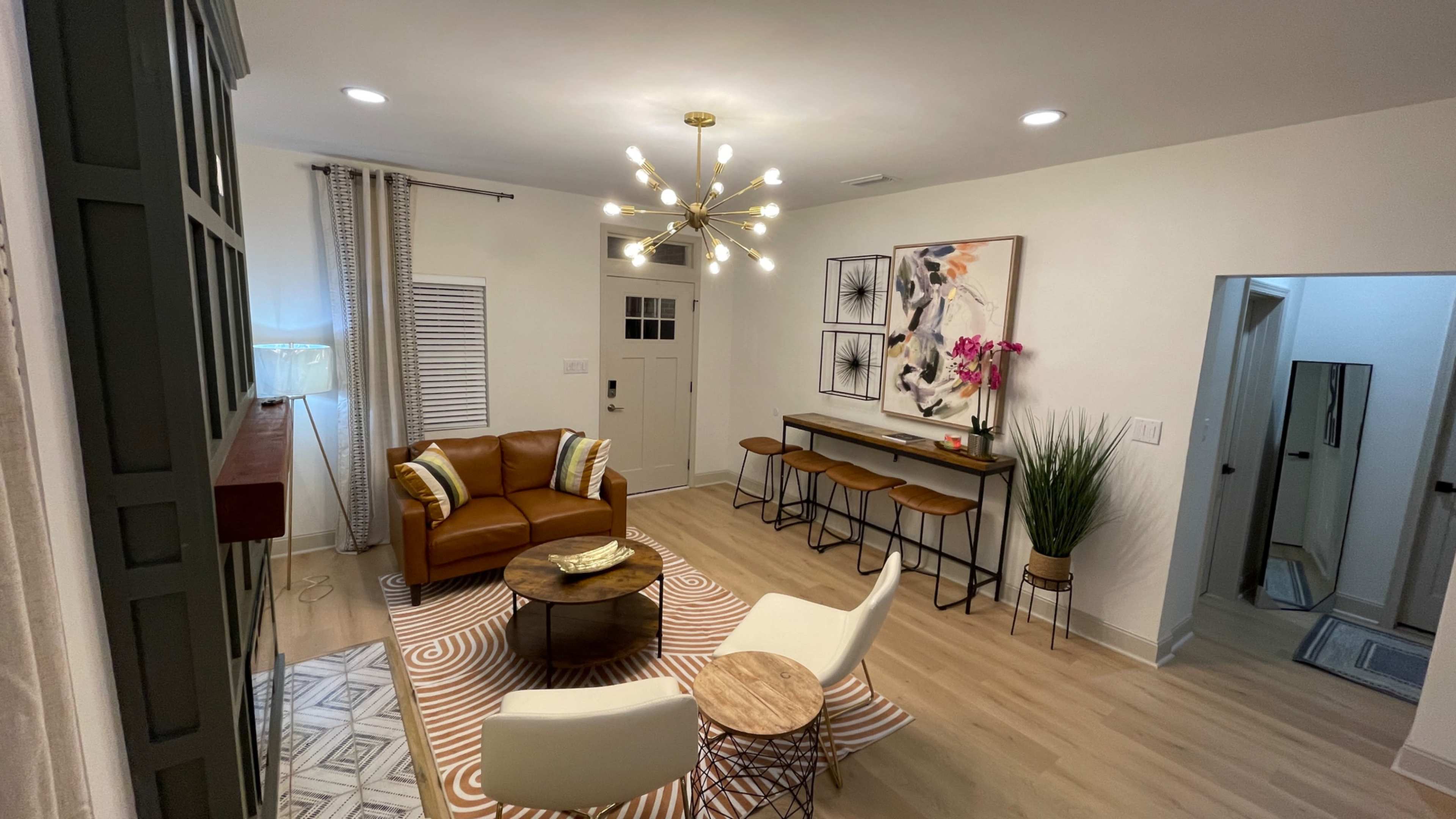 A modern living room featuring a brown leather sofa, a round coffee table, and a dining area with bar stools against a neutral backdrop.