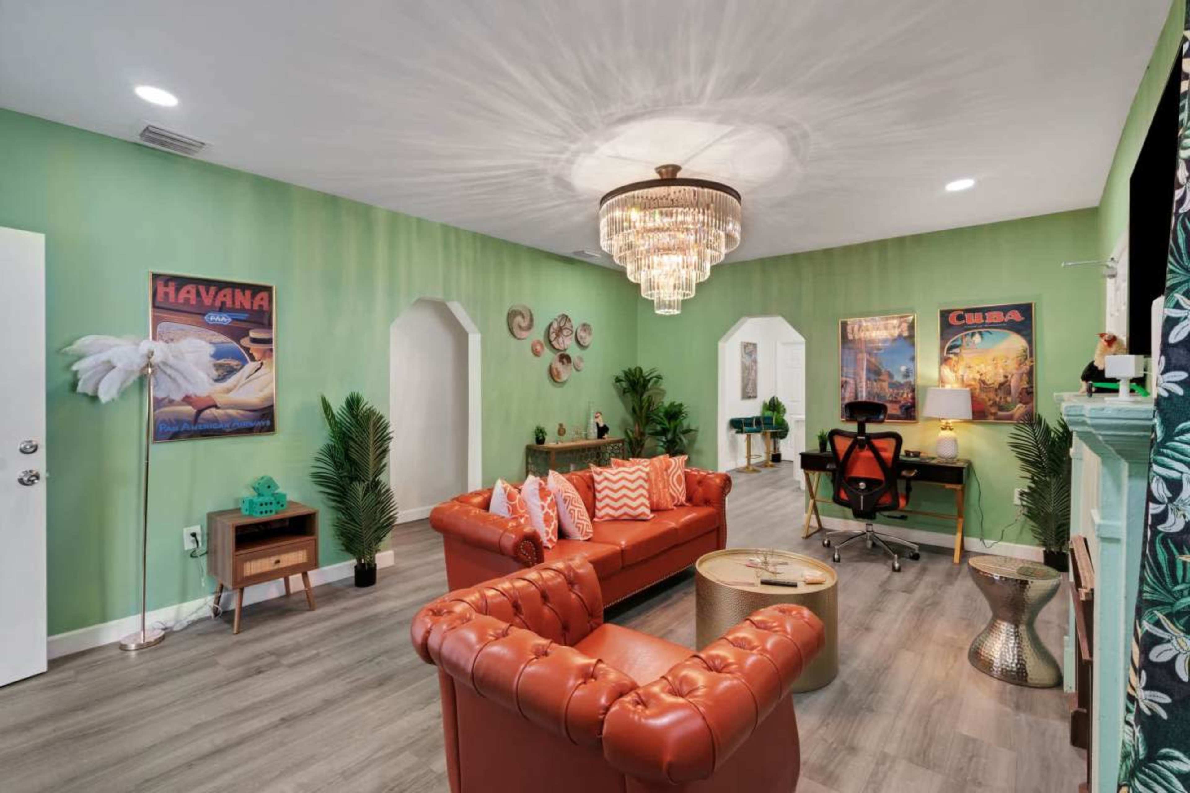 The image shows a vibrant living area featuring a brown leather sofa, green walls, decorative plants, and vintage Cuban posters.