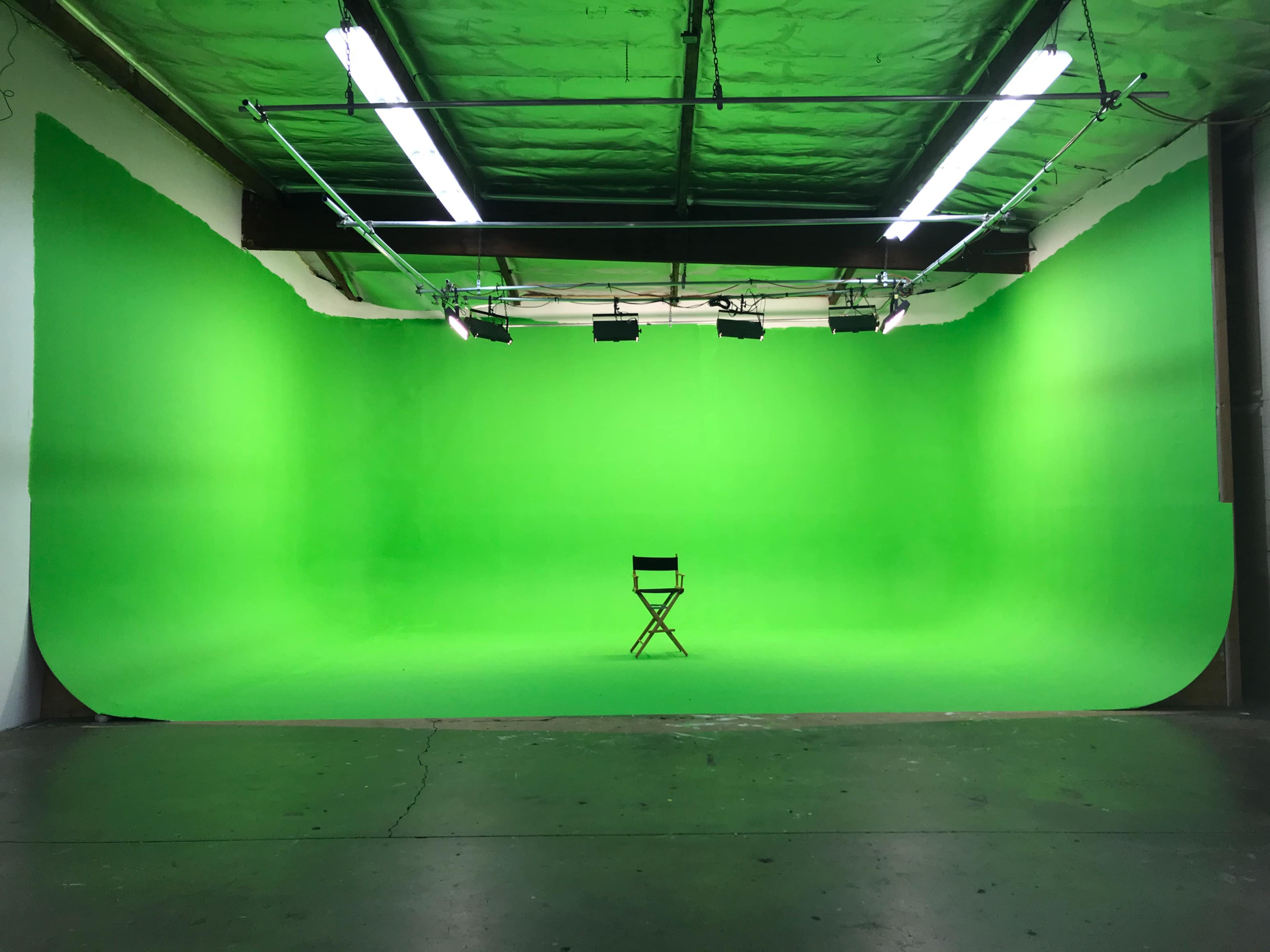 A green screen studio features a single director's chair centered in an empty space.