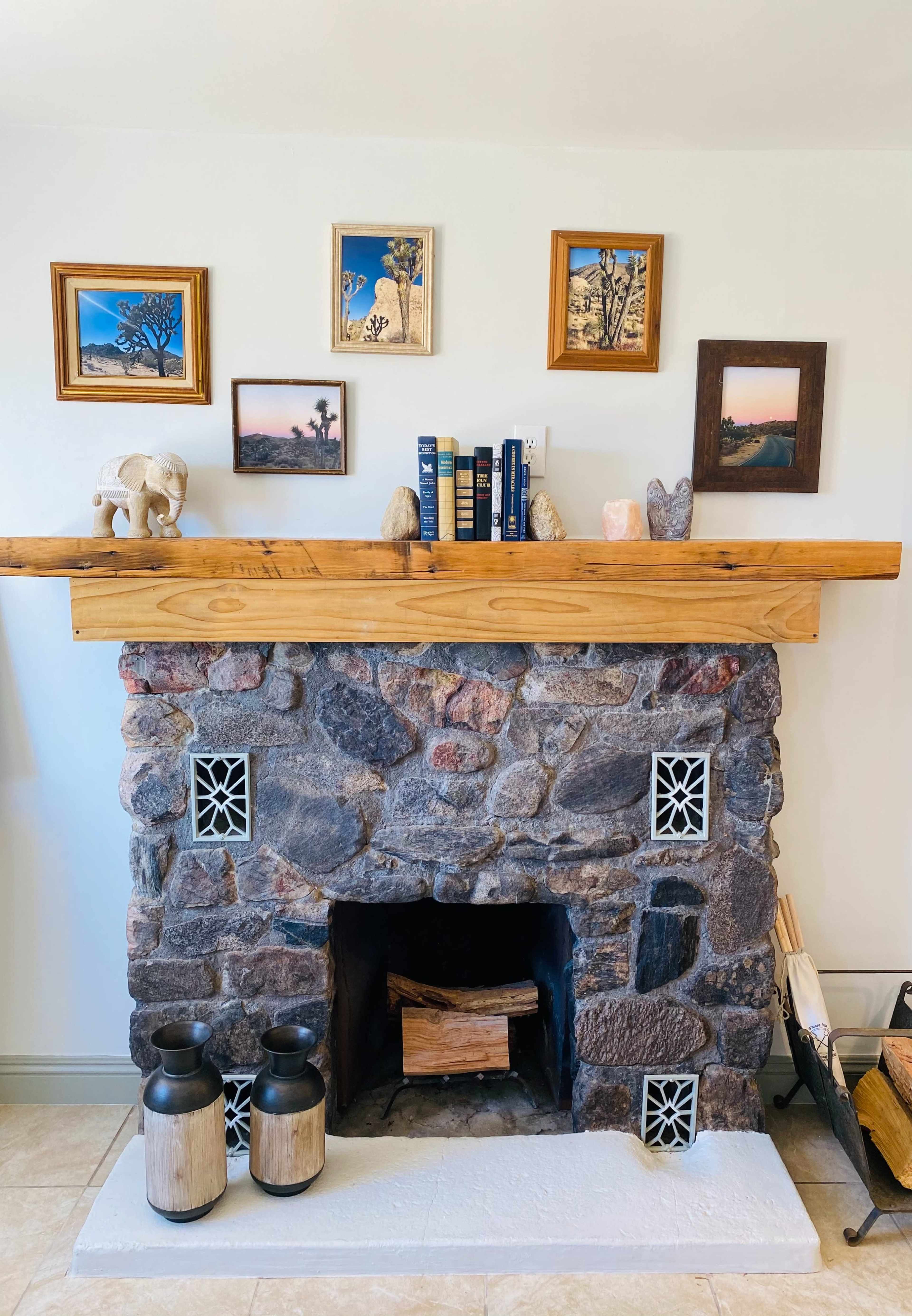 A stone fireplace with a wooden mantel displaying framed pictures, decorative objects, and two black lanterns beside it.
