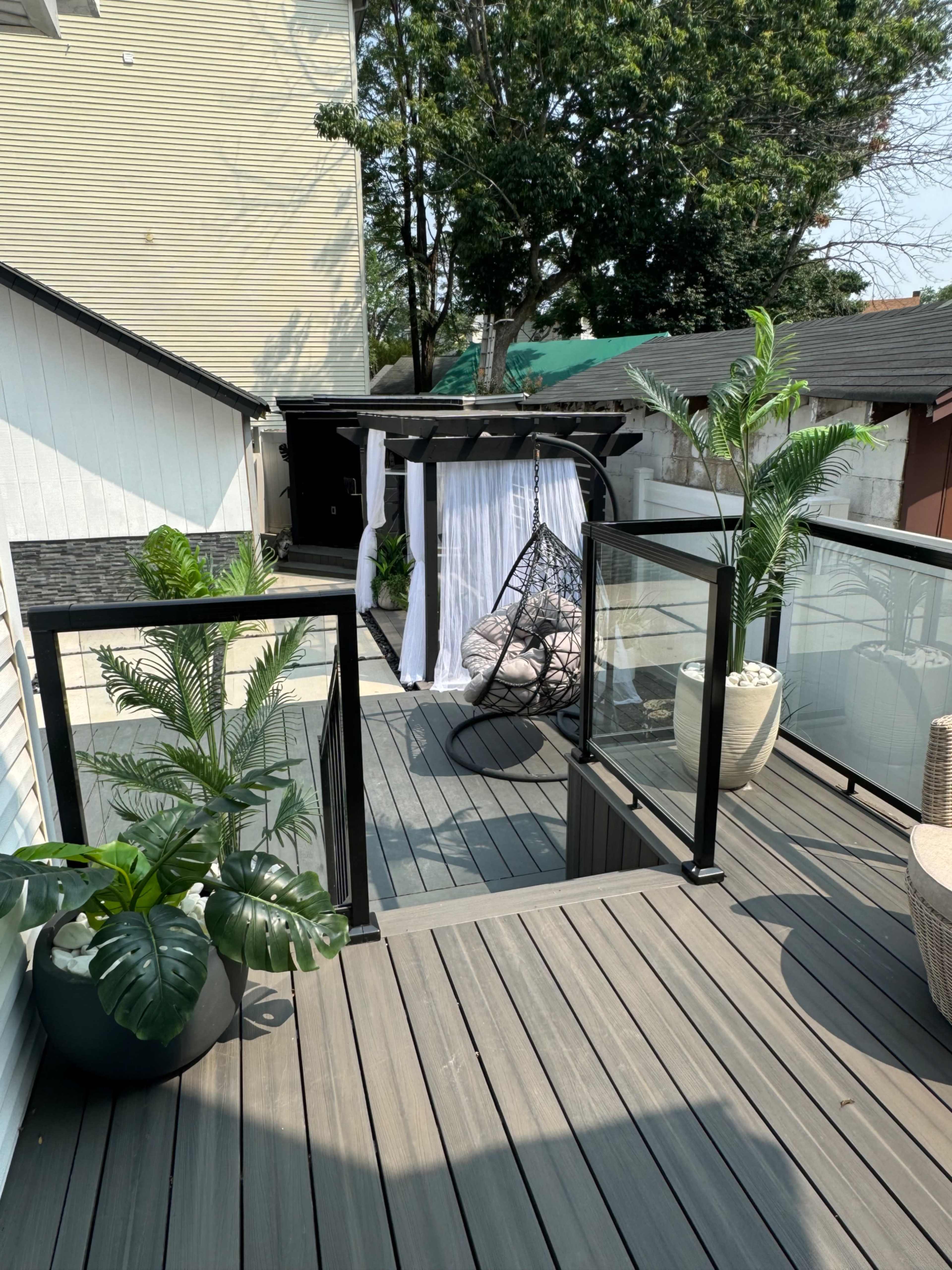 A spacious terrace features a hanging chair draped with white fabric, surrounded by potted plants and a glass railing.