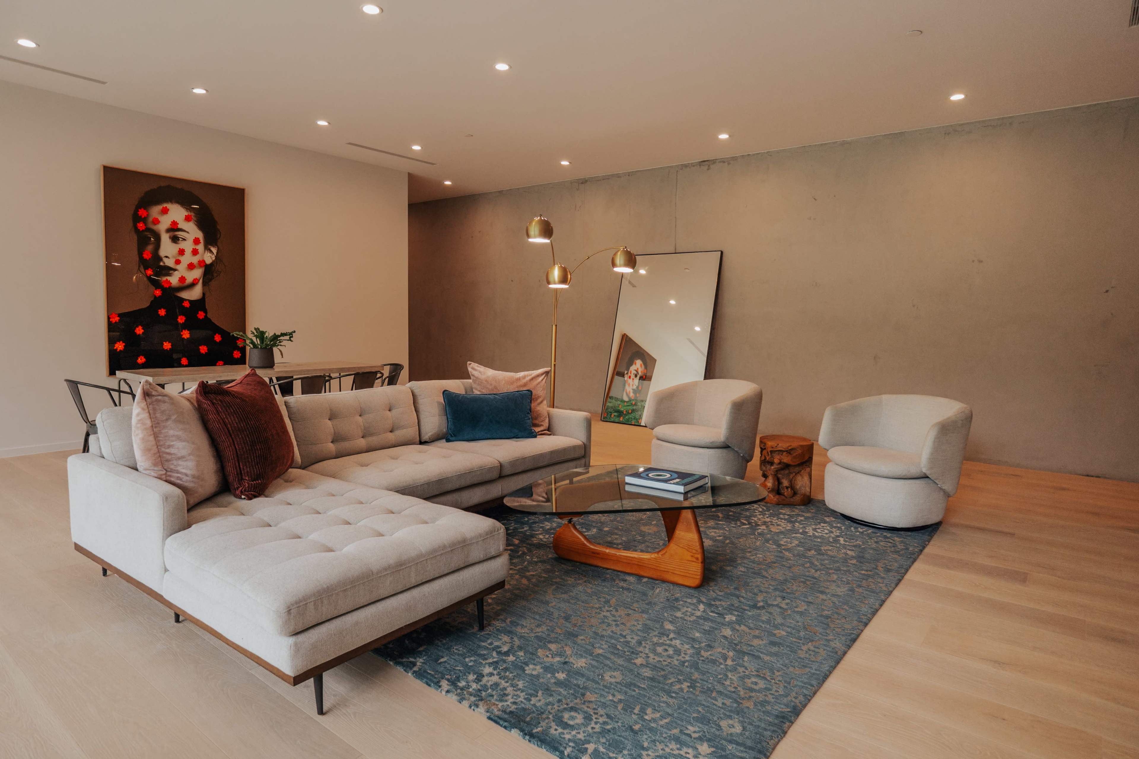The image shows a modern living room with a sectional sofa, a glass coffee table, and various artworks on the walls.
